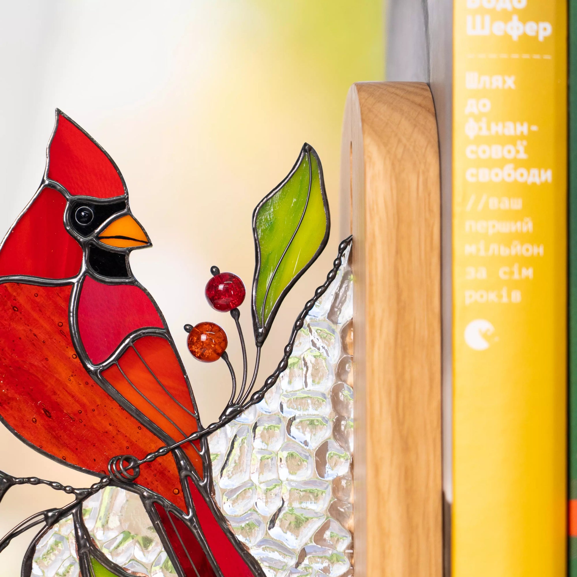 Stained glass cardinal bird artwork with a rich red glass body, black face markings, and orange beak, surrounded by green leaves and beads accents.