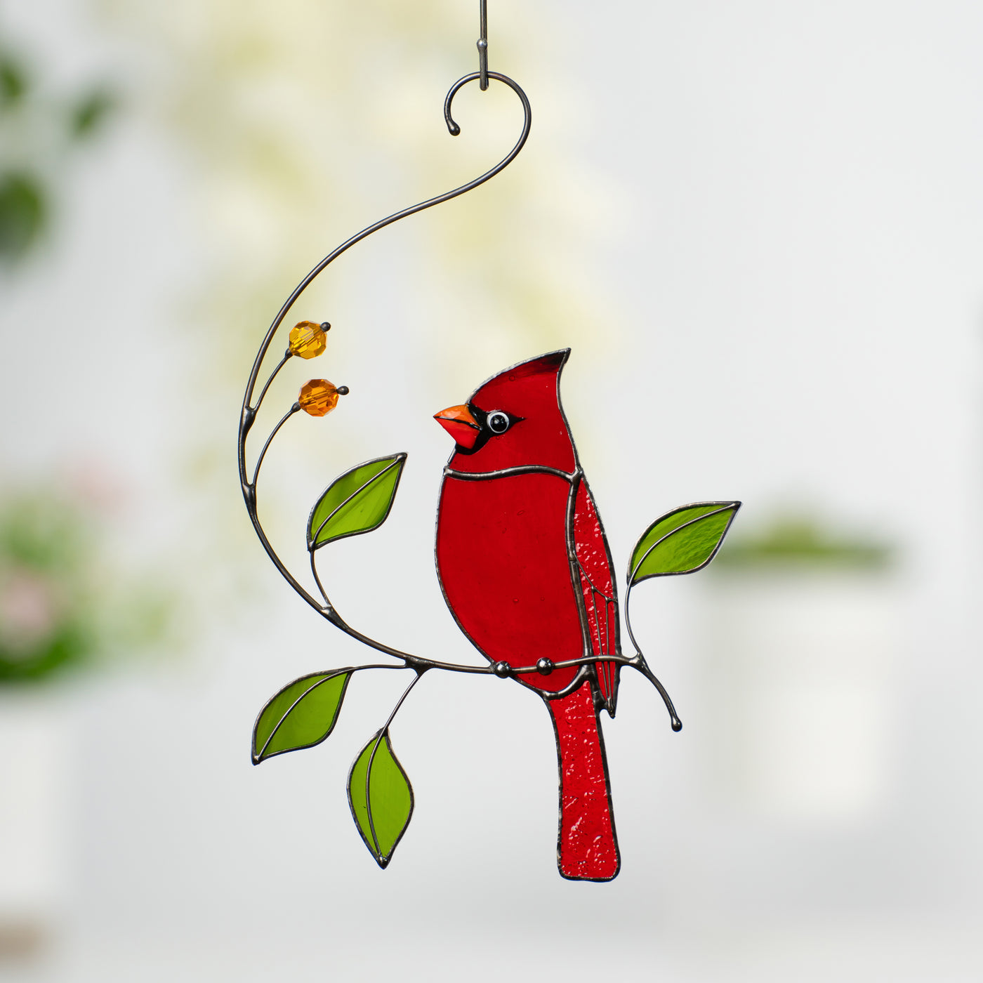 Handmade red cardinal glass bird hanging on a branch with yellow beads and green leaves