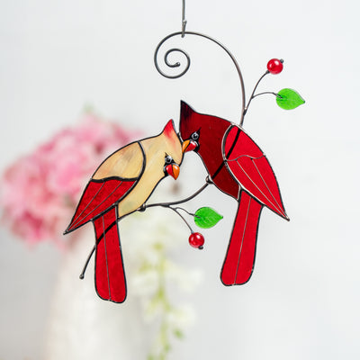 Close-up of stained glass cardinal with chain and green leaves, pastel wall art in background
