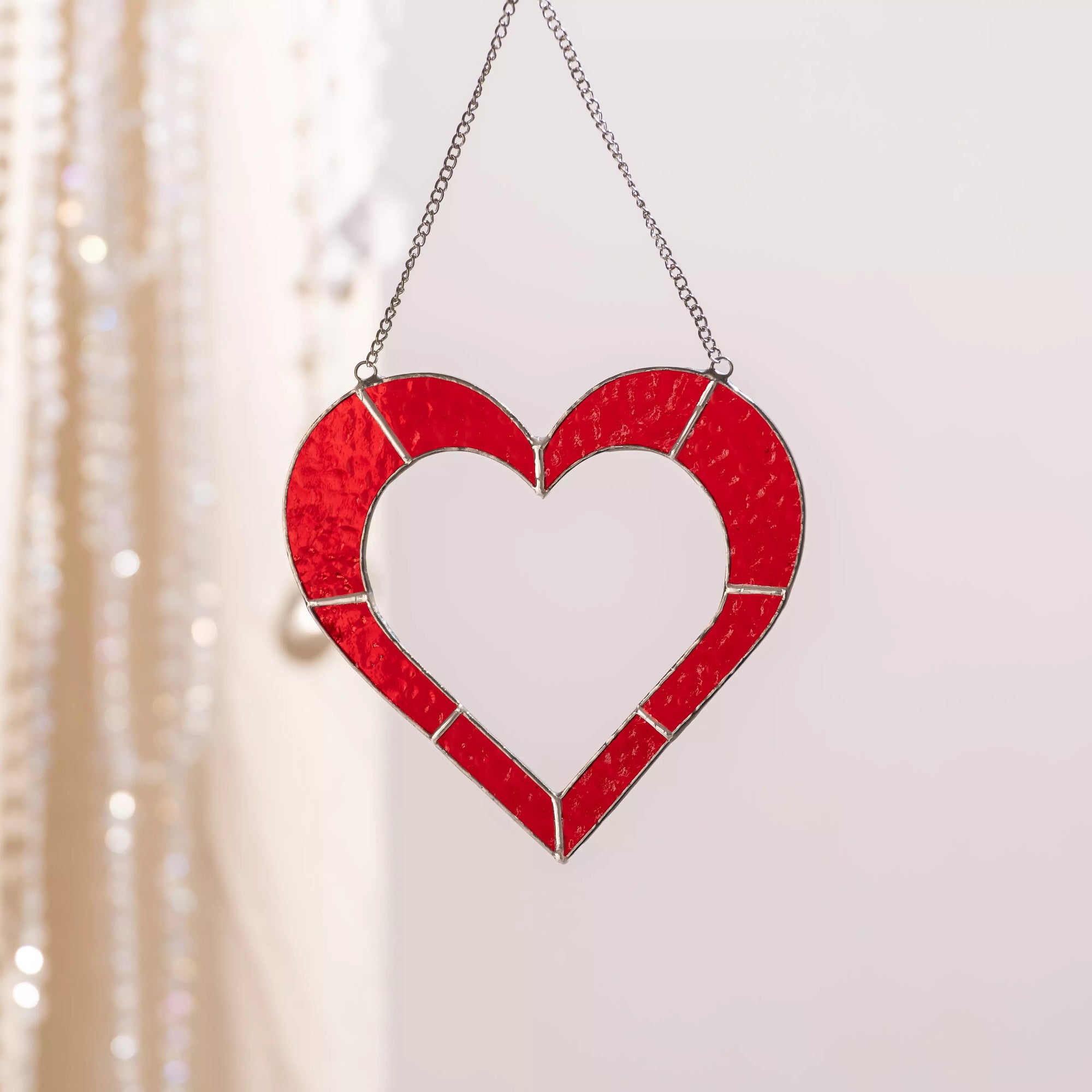 Handmade red stained glass heart suncatcher hanging indoors, highlighting its rich red color and textured glass.