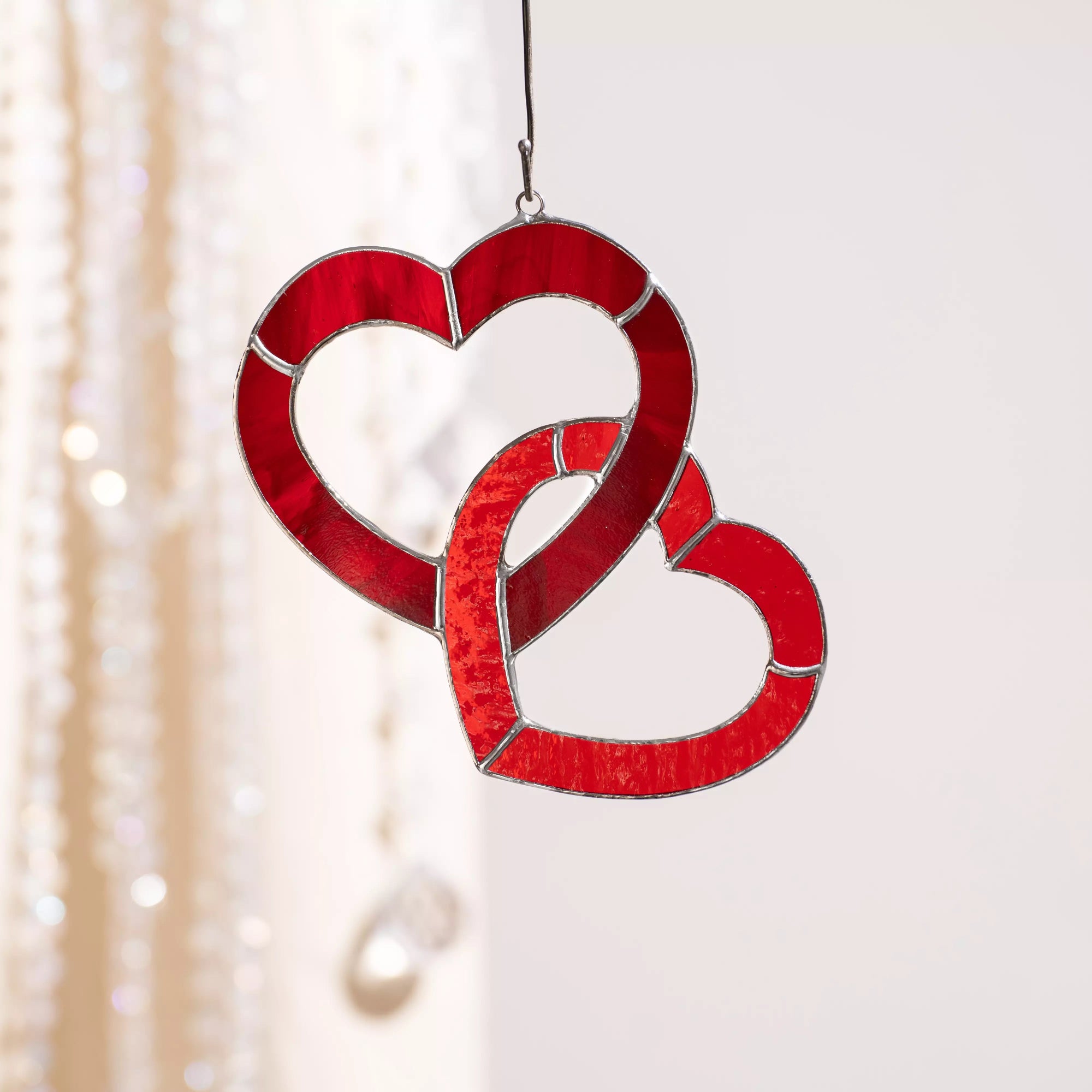 Red stained glass double heart suncatcher hanging on a cord, made of deep ruby glass with silver solder lines.