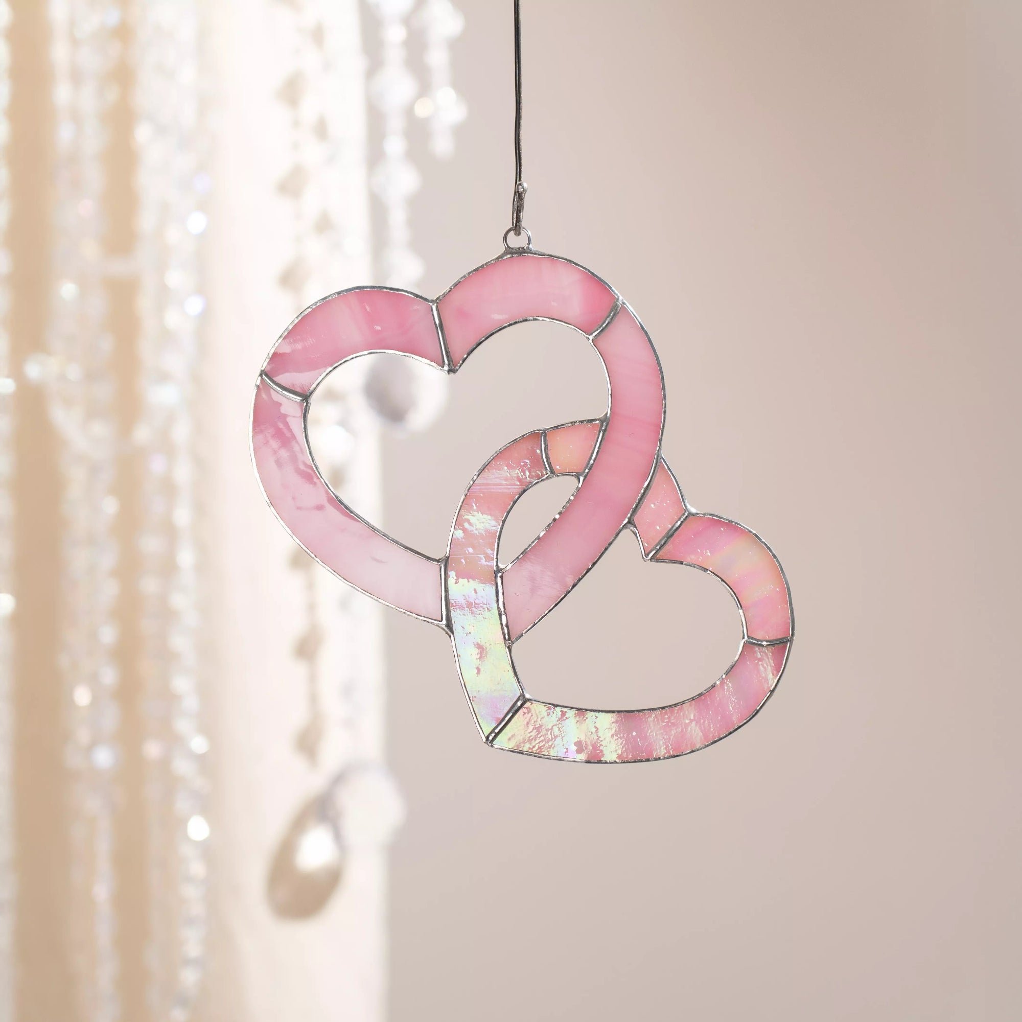 Pink stained glass heart suncatcher hanging indoors on a cord, glowing softly in natural light.
