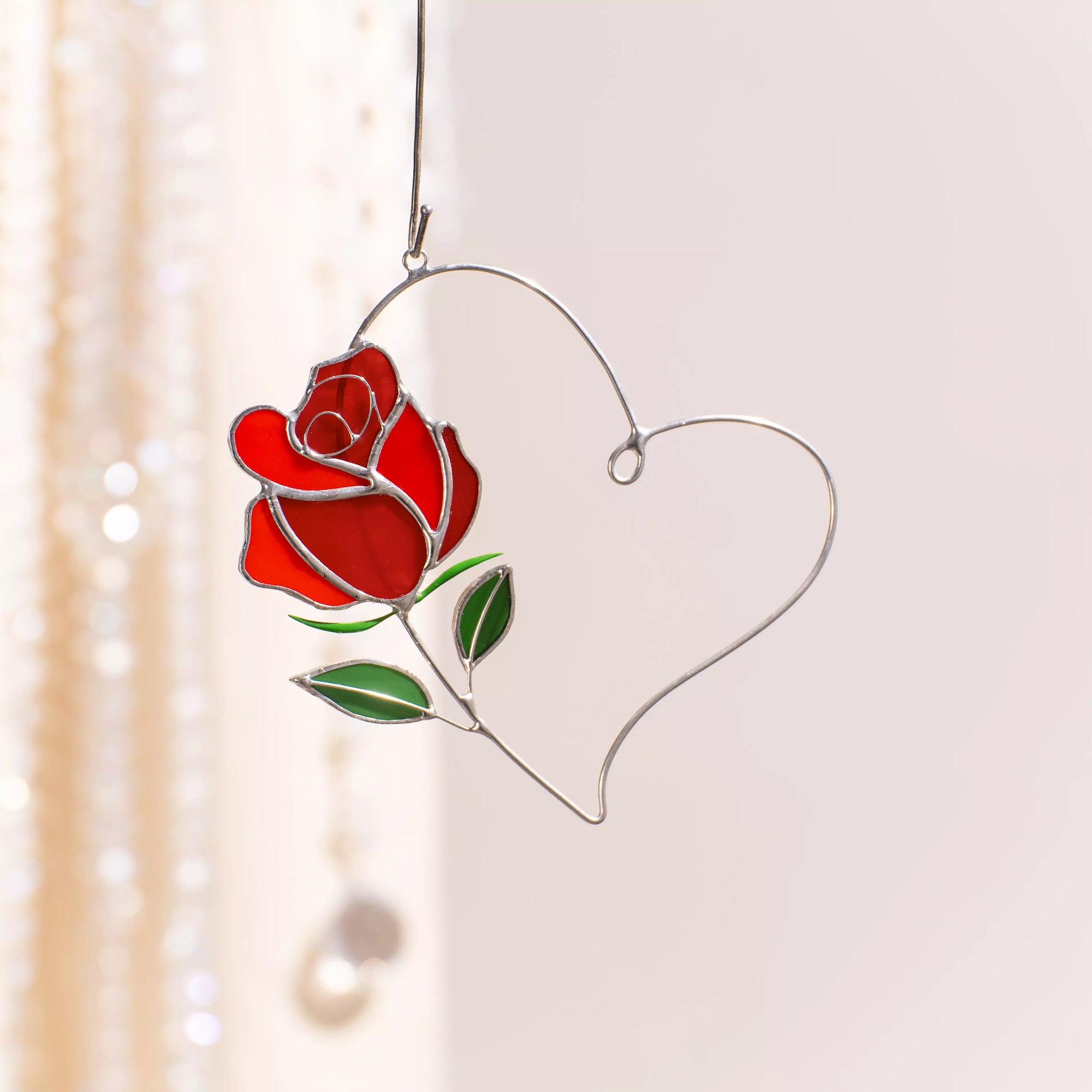 Rose heart stained glass suncatcher hanging by a ribbon in a softly lit interior.