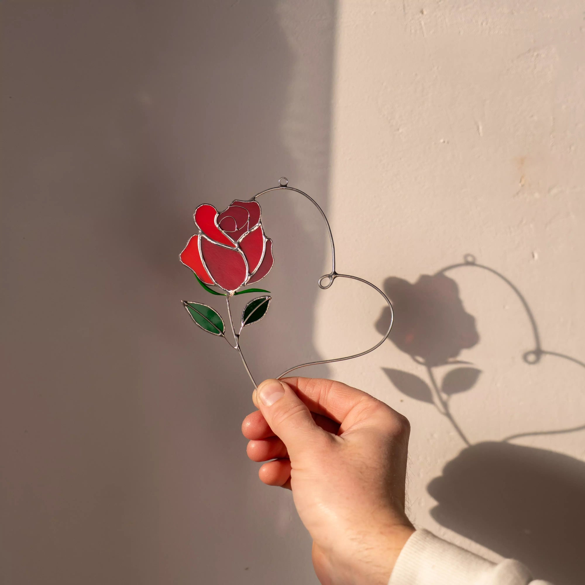 Rose heart stained glass suncatcher catching sunlight and casting a soft floral shadow on the wall.