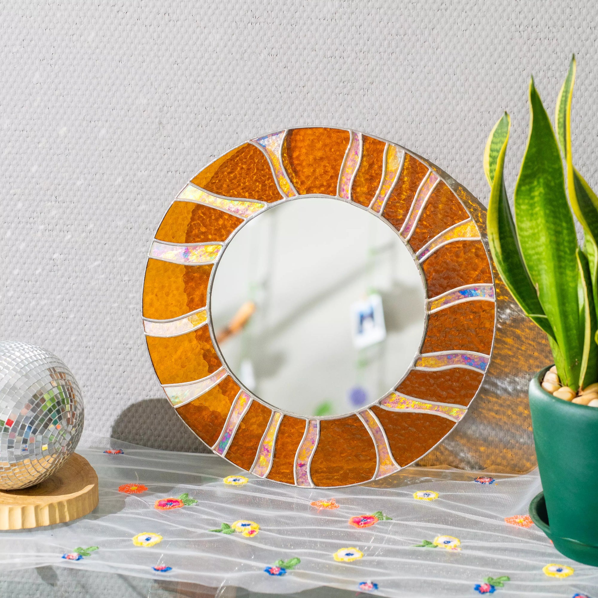 Stained glass round mirror with orange and brown colors on a decorative table.
