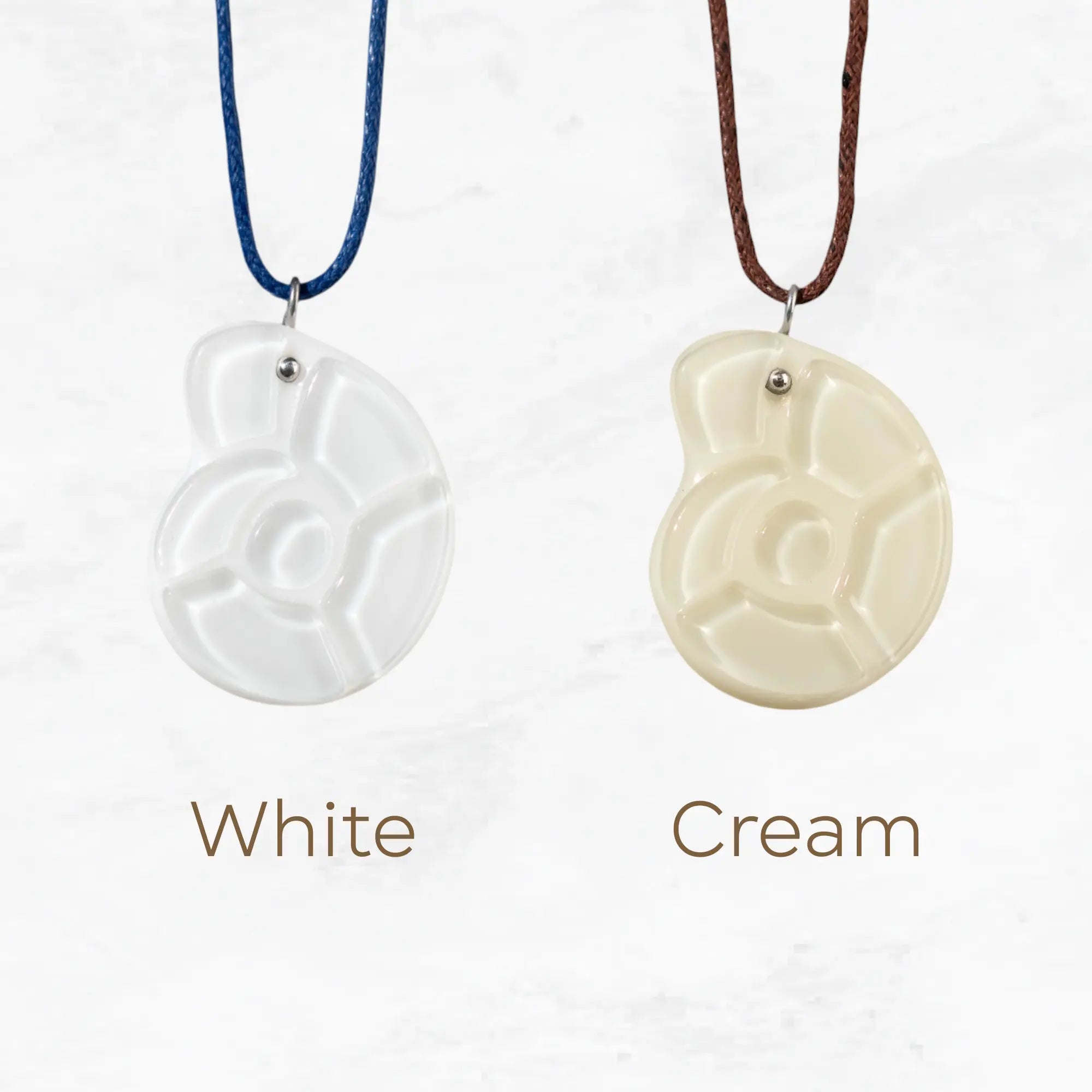 Two stained glass nautilus pendants — one in white with a blue cord, one in cream with a brown cord. 