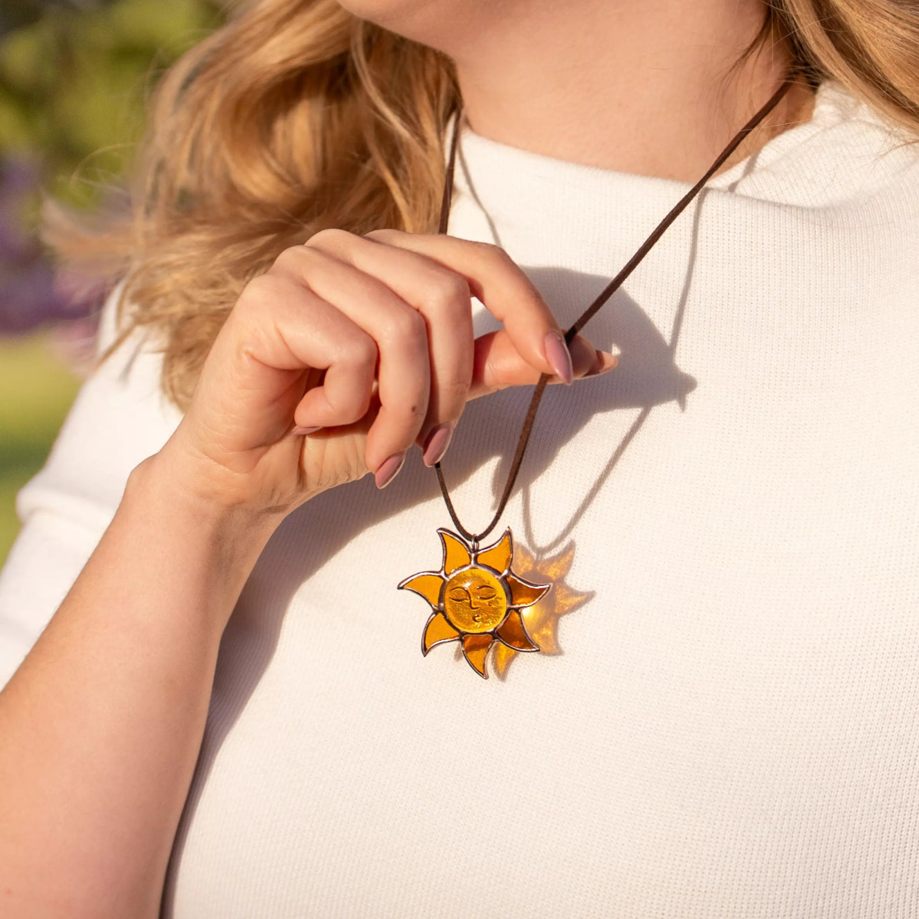 Woman in sunlight wearing amber stained glass sun necklace on vegan suede cord, close-up outdoor shot