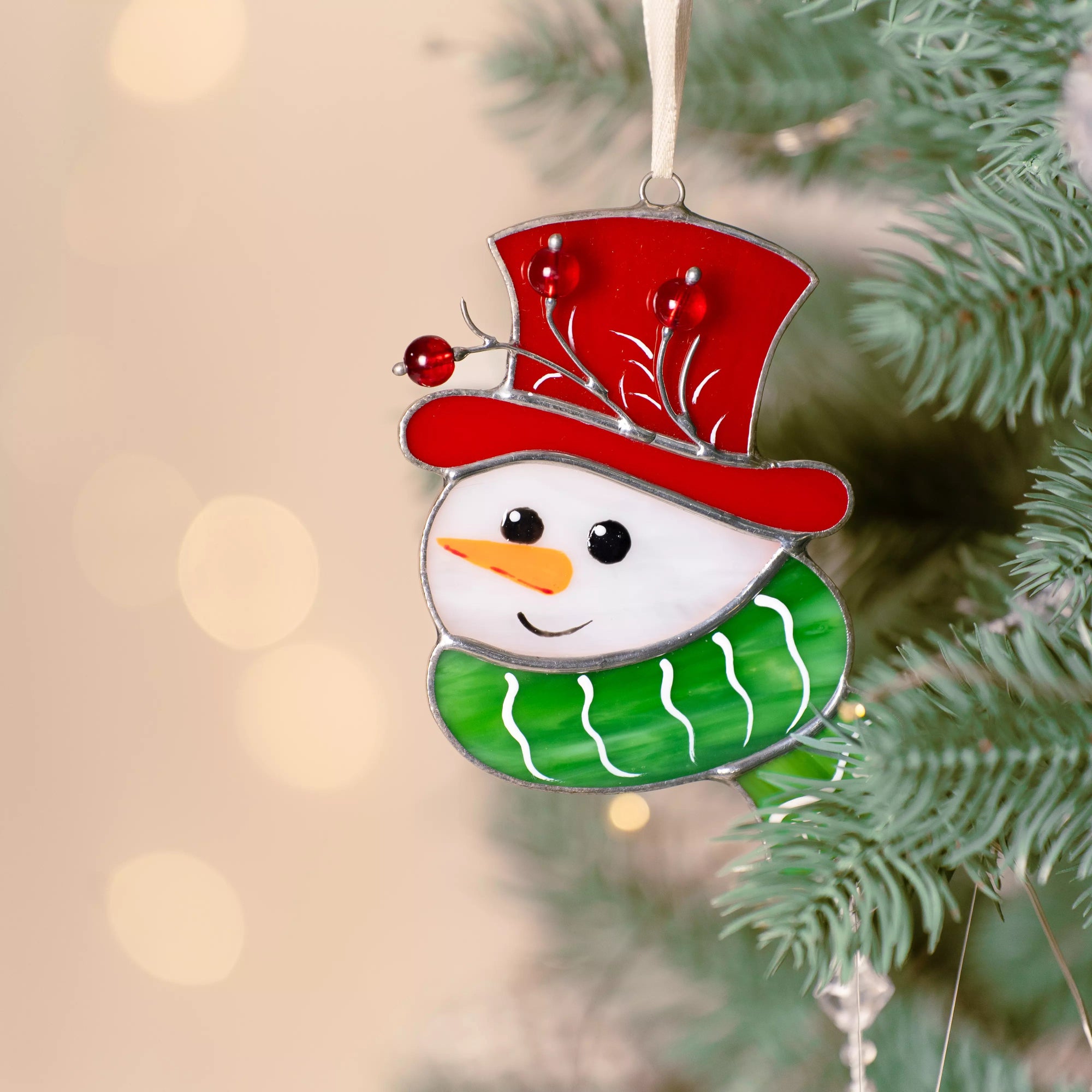 Close-up of a snowman stained glass ornament hanging on a Christmas tree with soft festive lights.