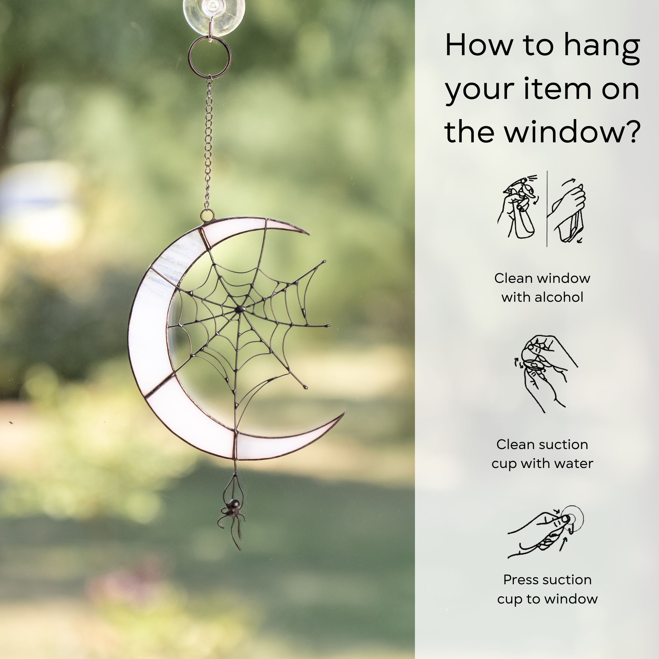 Stained glass spider moon hanging on a window, sunlight enhancing the web and crescent details, instruction beside: clean window and suction cup, press a cup to the surface