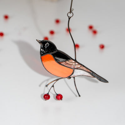 Glass suncatcher American robin with orange and black coloring, decorated with red glass beads, placed on a white surface.