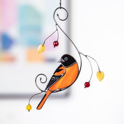 Baltimore oriole stained glass suncatcher hanging in front of abstract art, decorated with red beads and yellow glass leaves