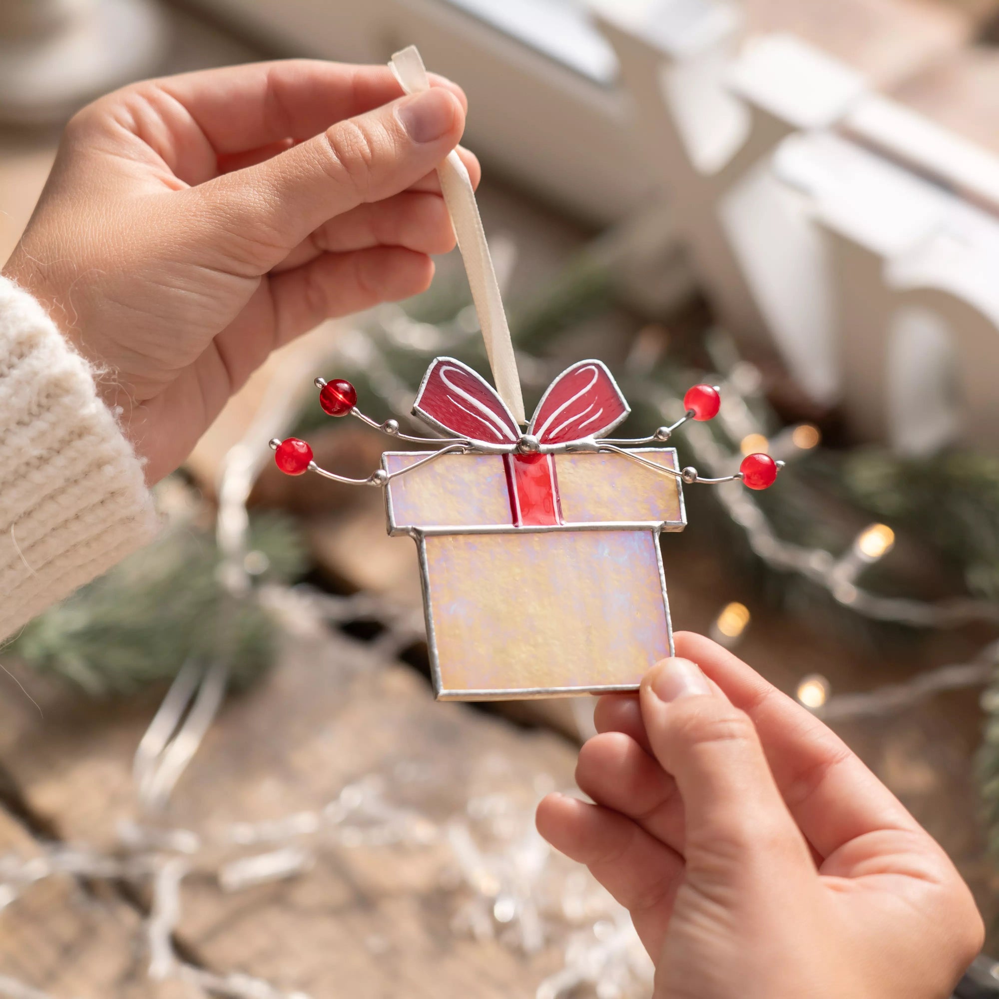 Hands holding a Christmas gift box stained glass ornament with red bow and red beads