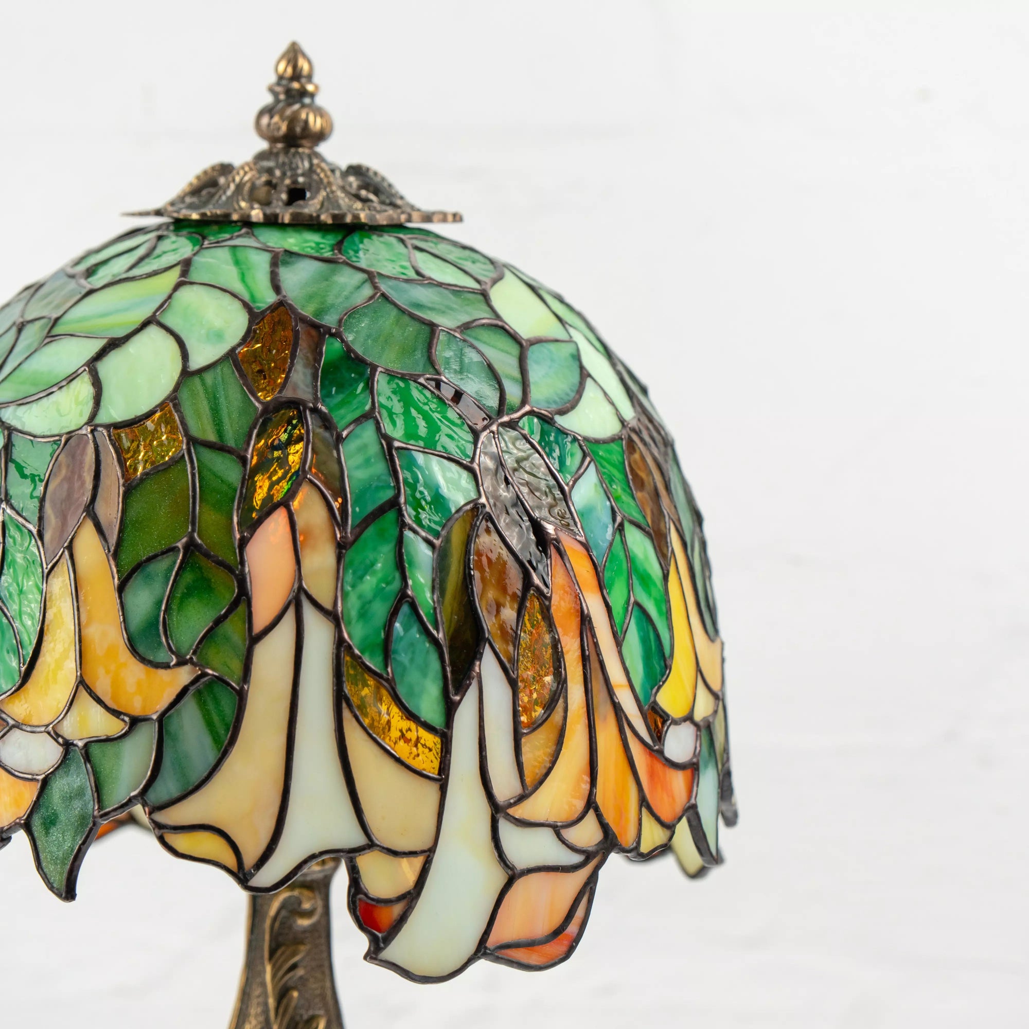 Detailed close-up of stained glass lamp shade showing layered green leaves and golden trumpet flowers with warm glow.