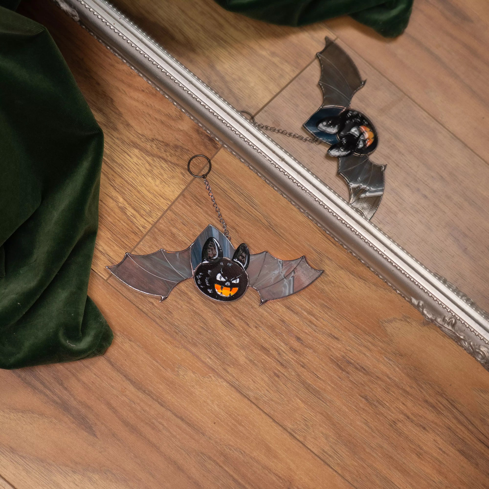 Stained glass bat with grey wings and fangs lying by mirror