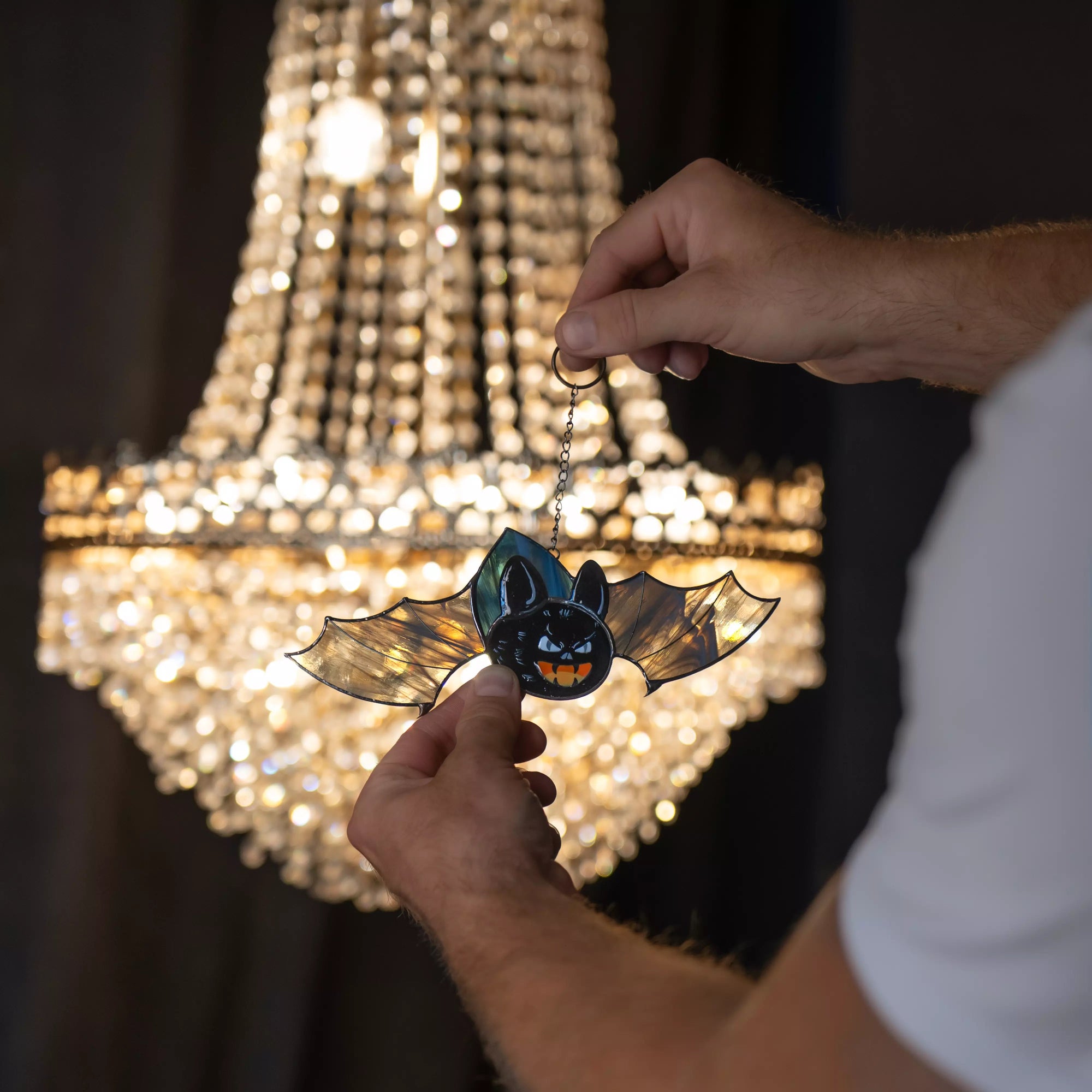 Stained glass bat suncatcher with grey wings held near chandelier light