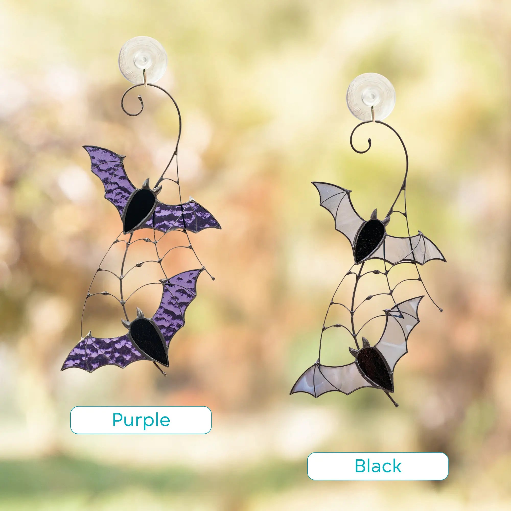 Two bat-shaped window decorations with purple and black color variation on a blurred natural background.