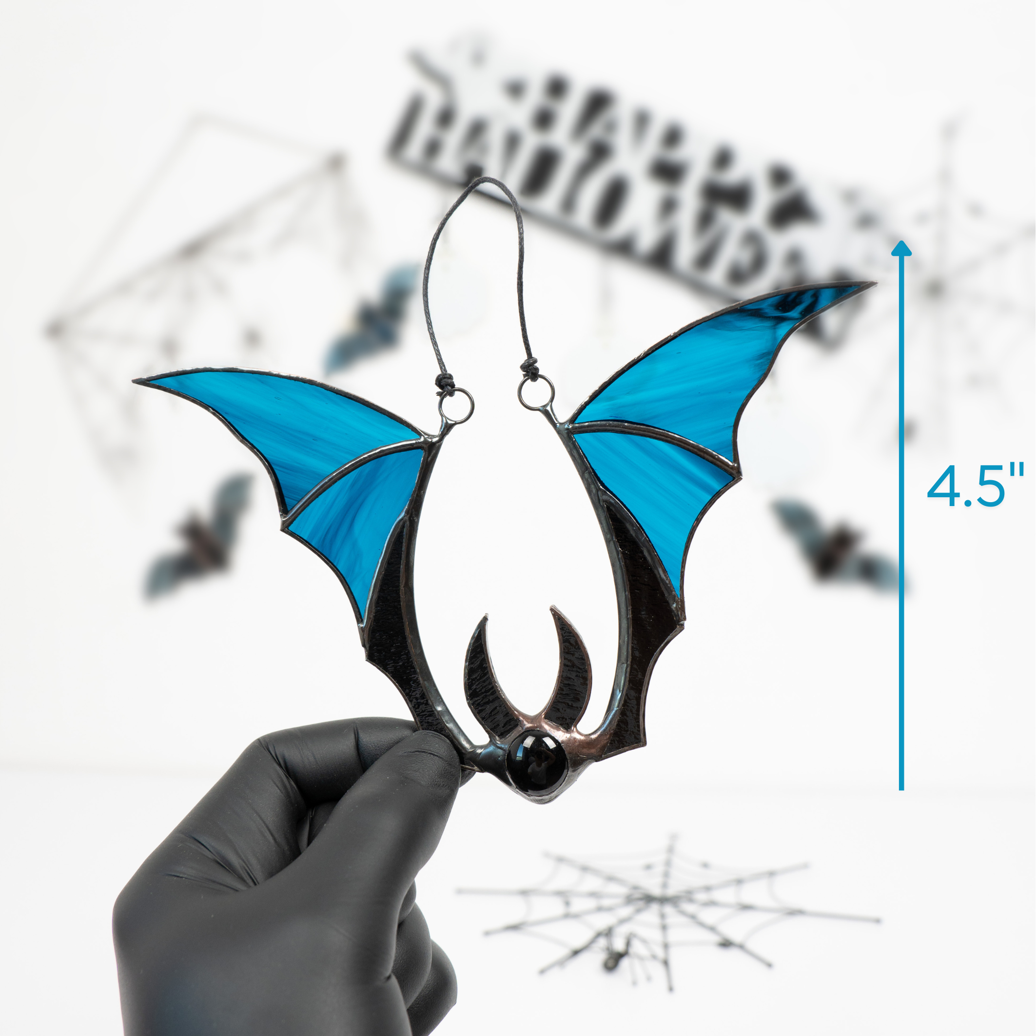 A person holding blue-winged bat suncatcher, with 4.5" height text and Halloween background.