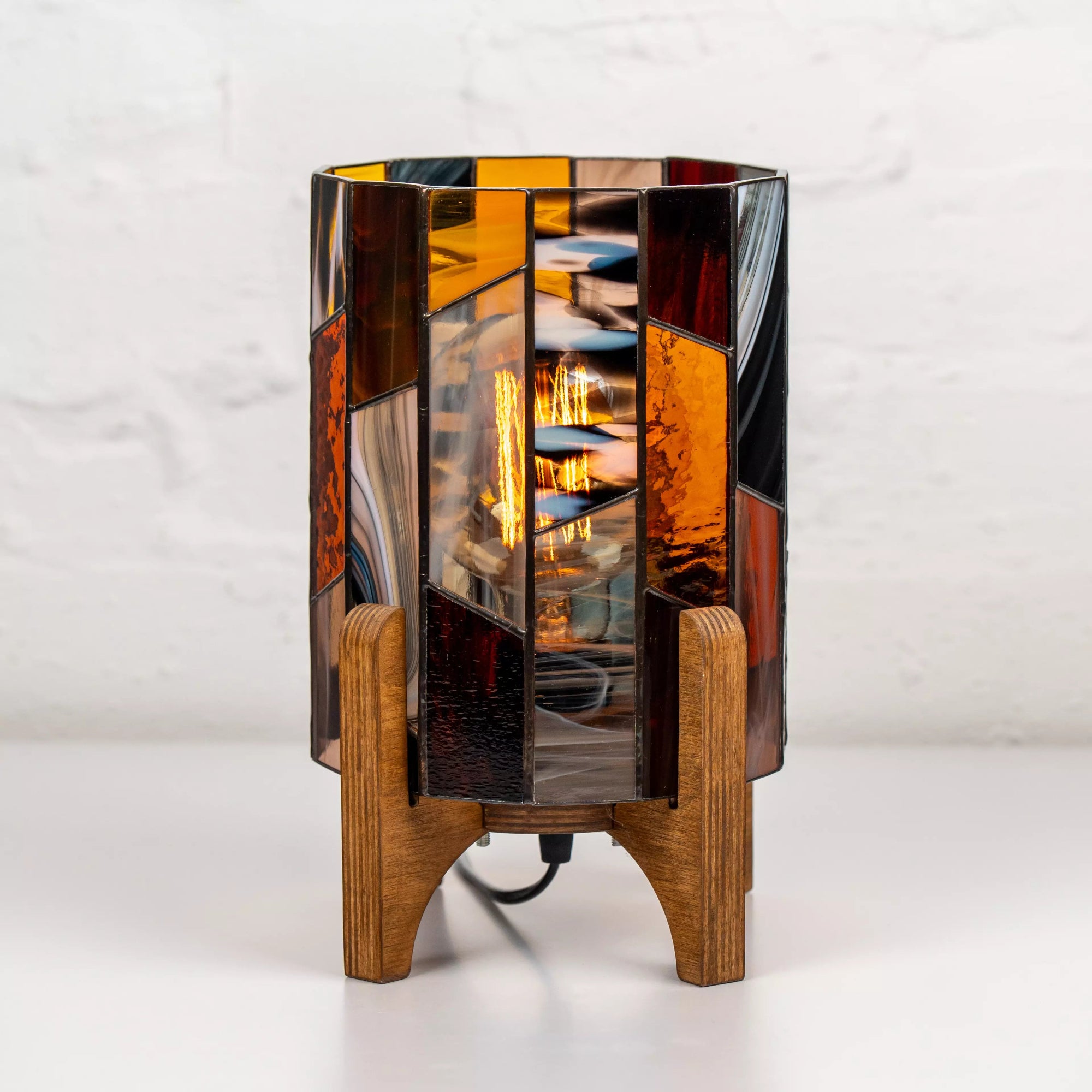 Stained glass bedside lamp with Edison bulb and geometric amber glass, standing on a natural wood base, perfect for cozy home decor.