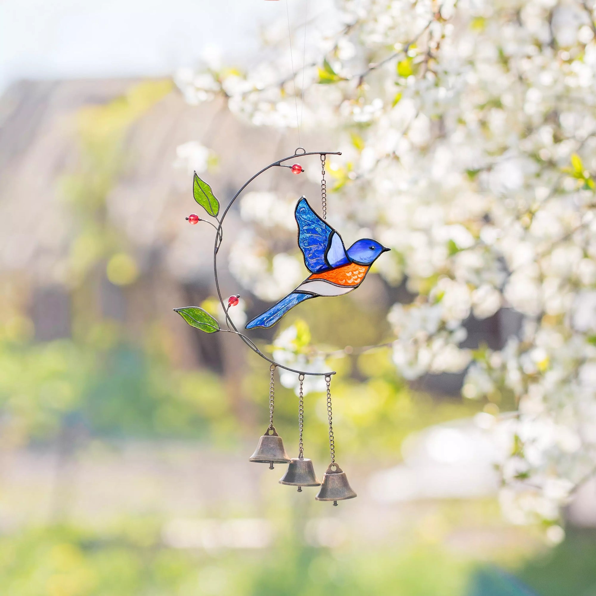 Stained glass bluebird windchime with bells against a blurred natural background