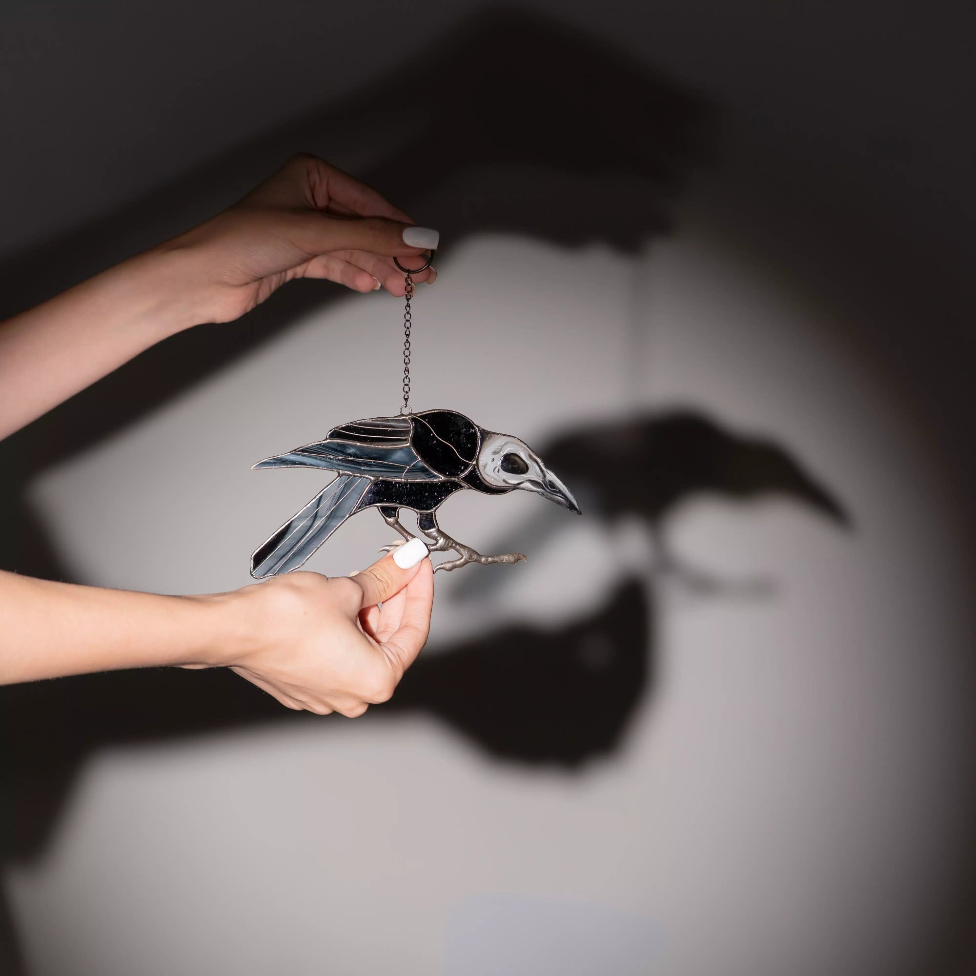 Stained glass raven suncatcher held by a hand with a sharp shadow on the wall