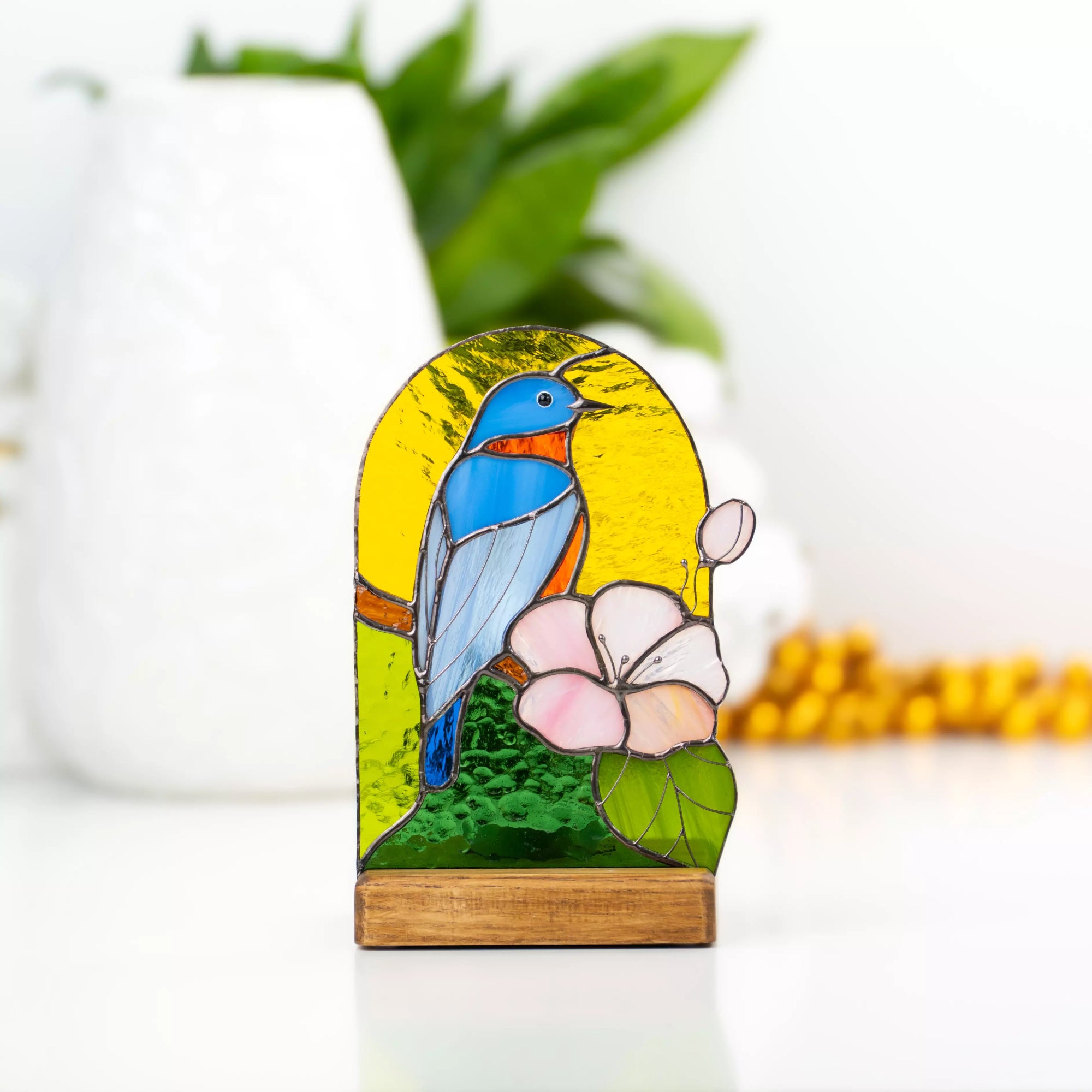 Stained glass panel with a blue bird and pink flower on a wooden stand, blurred background