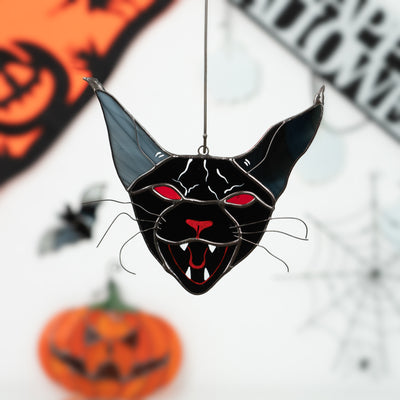 Black stained glass cat with red eyes and fangs hanging as Halloween decor, surrounded by bats, pumpkins, and webs.
