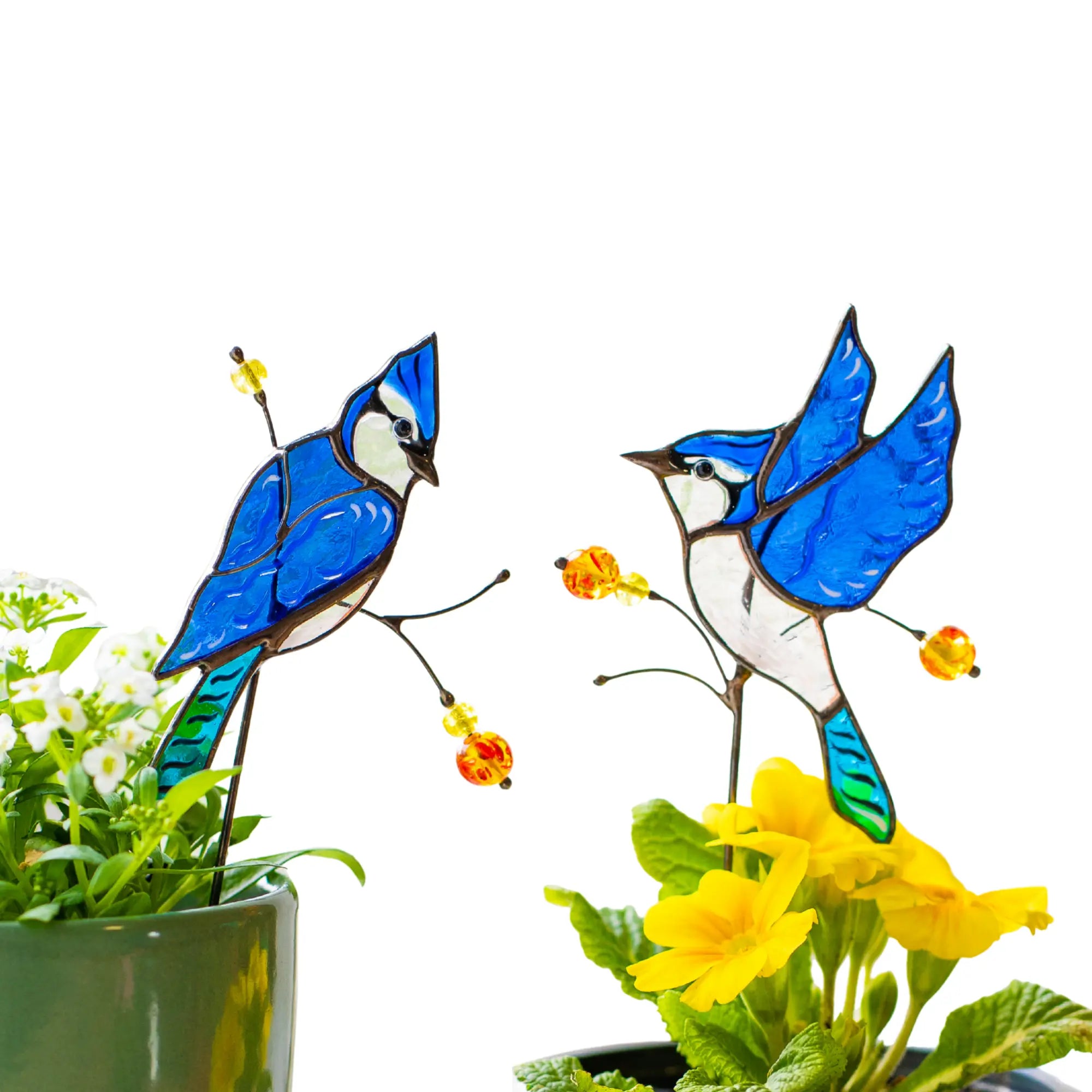 Stained glass blue jay plant stakes in a garden setting with flowers and plants.