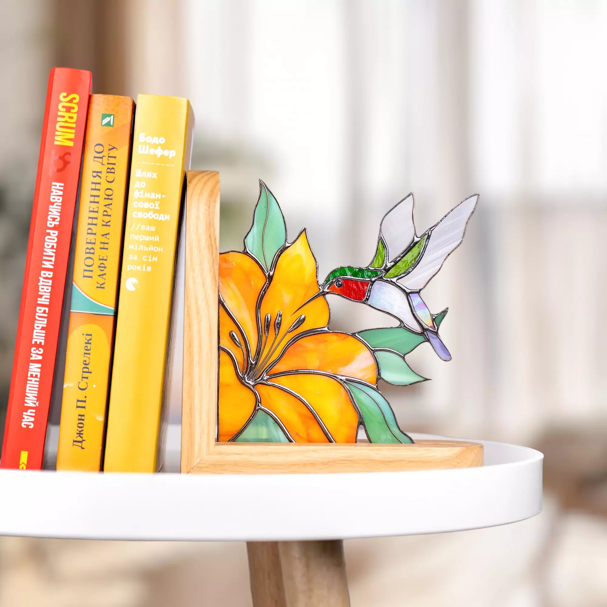 Stained glass hummingbird flying toward orange flower in wooden bookend on table