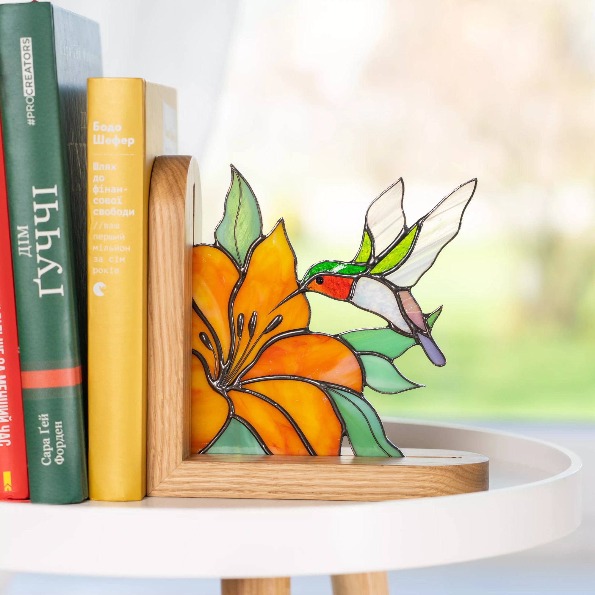 Stained glass hummingbird flying to orange flower bookend displayed on white round table