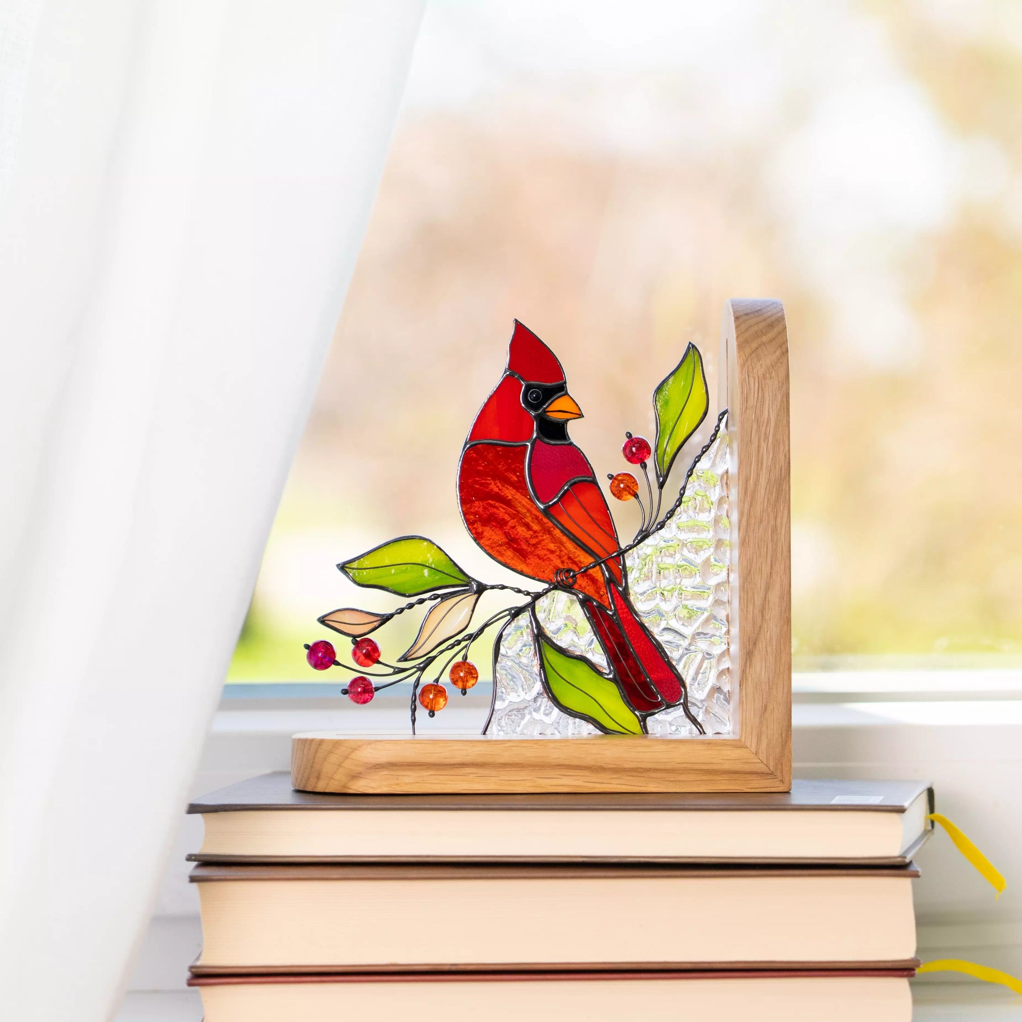 Stained glass bookend panel of a cardinal bird on a branch with leaves and berries, placed on books.