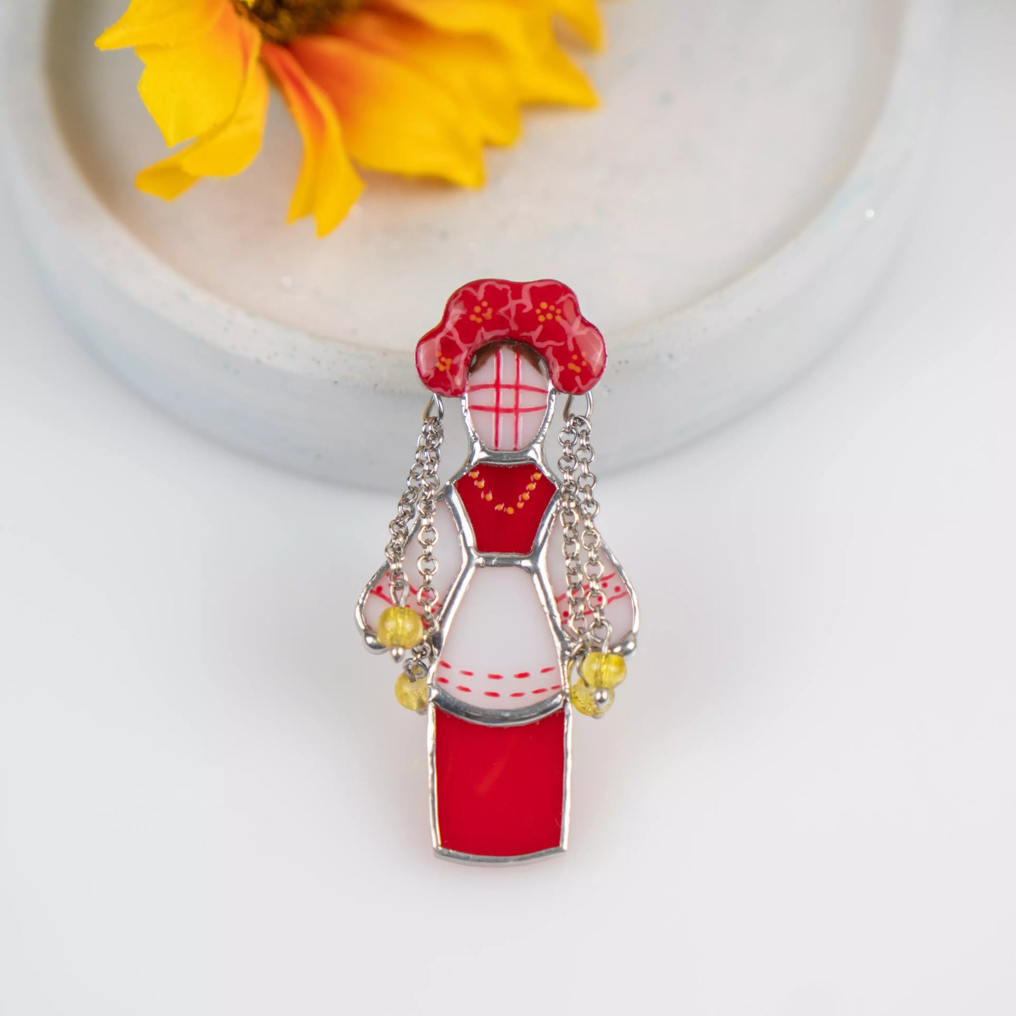 Stained glass brooch featuring traditional ukrainian guardian doll in white and red colors