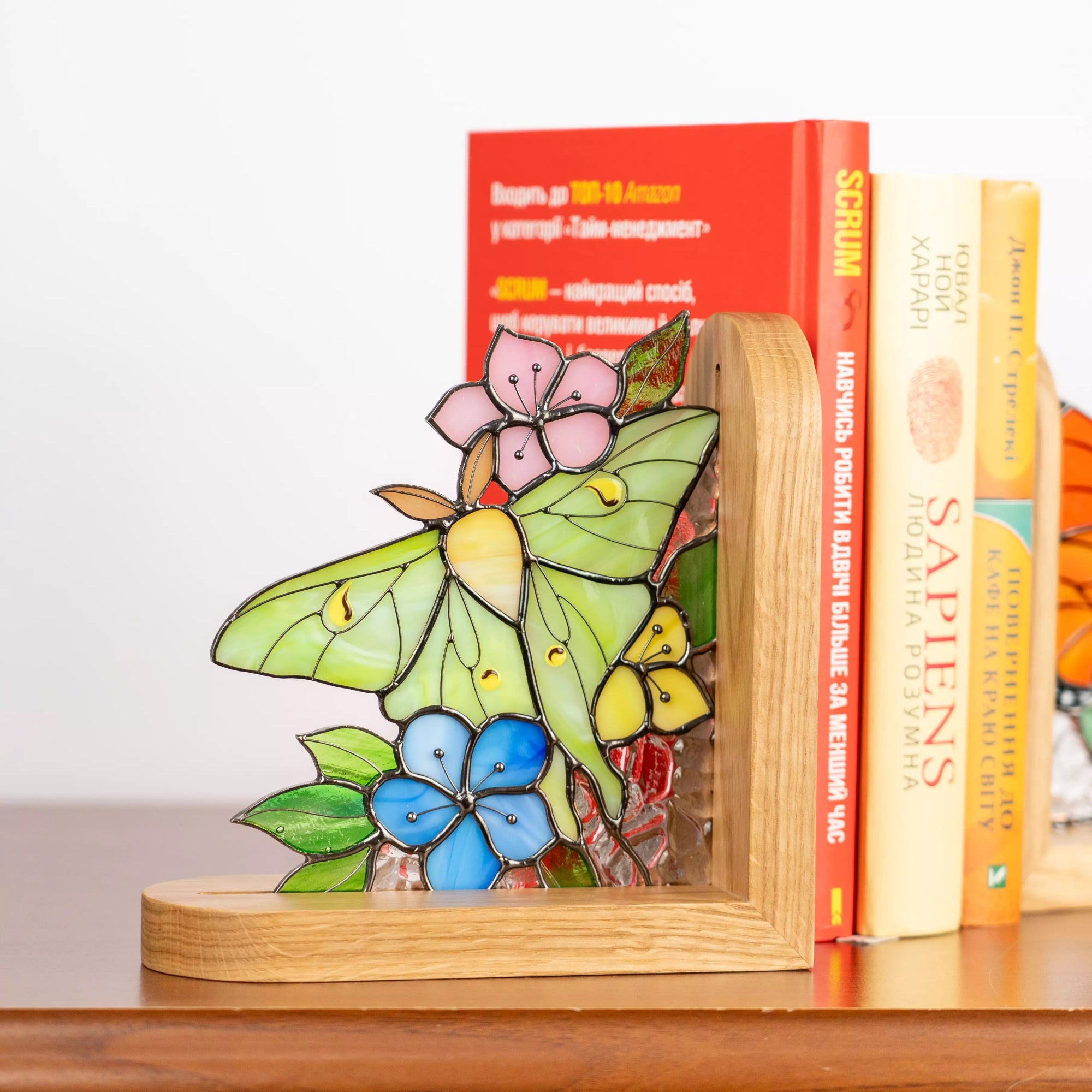 Stained glass butterfly bookend with green wings and floral design on wooden surface near books