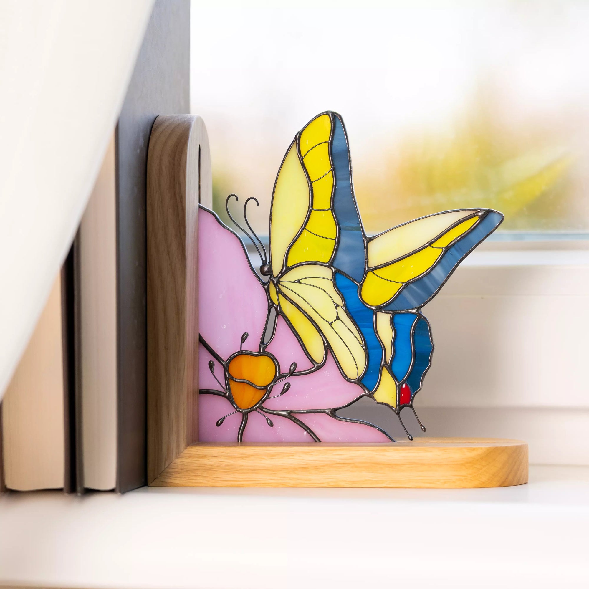 Stained glass butterfly bookend standing in a wooden holder near a window