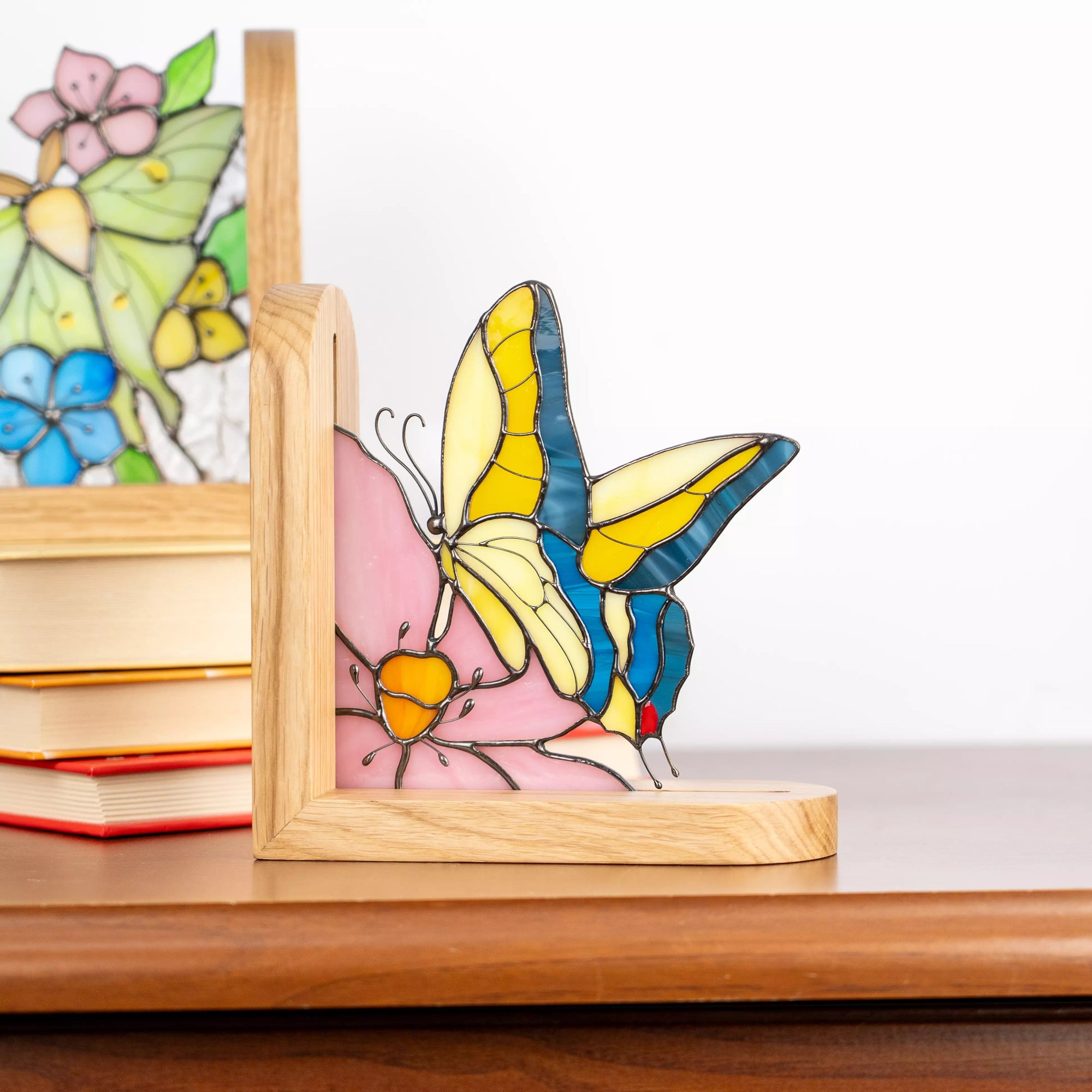 Handcrafted stained glass butterfly bookend displayed on a shelf, featuring yellow, blue, and pink glass with a smooth wooden base, styled as elegant home decor.