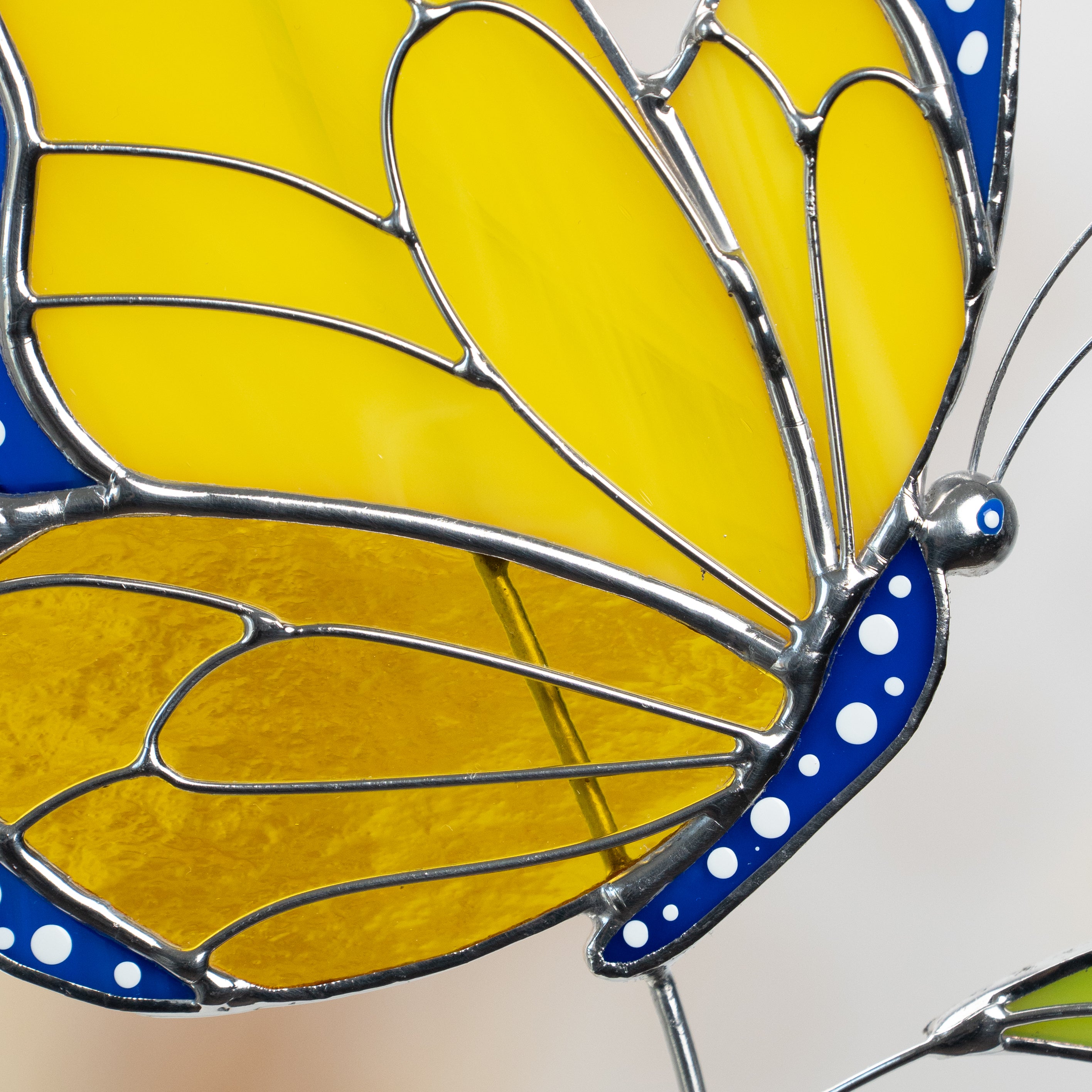 Close-up of stained glass butterfly wing with yellow glass and blue dotted edge.