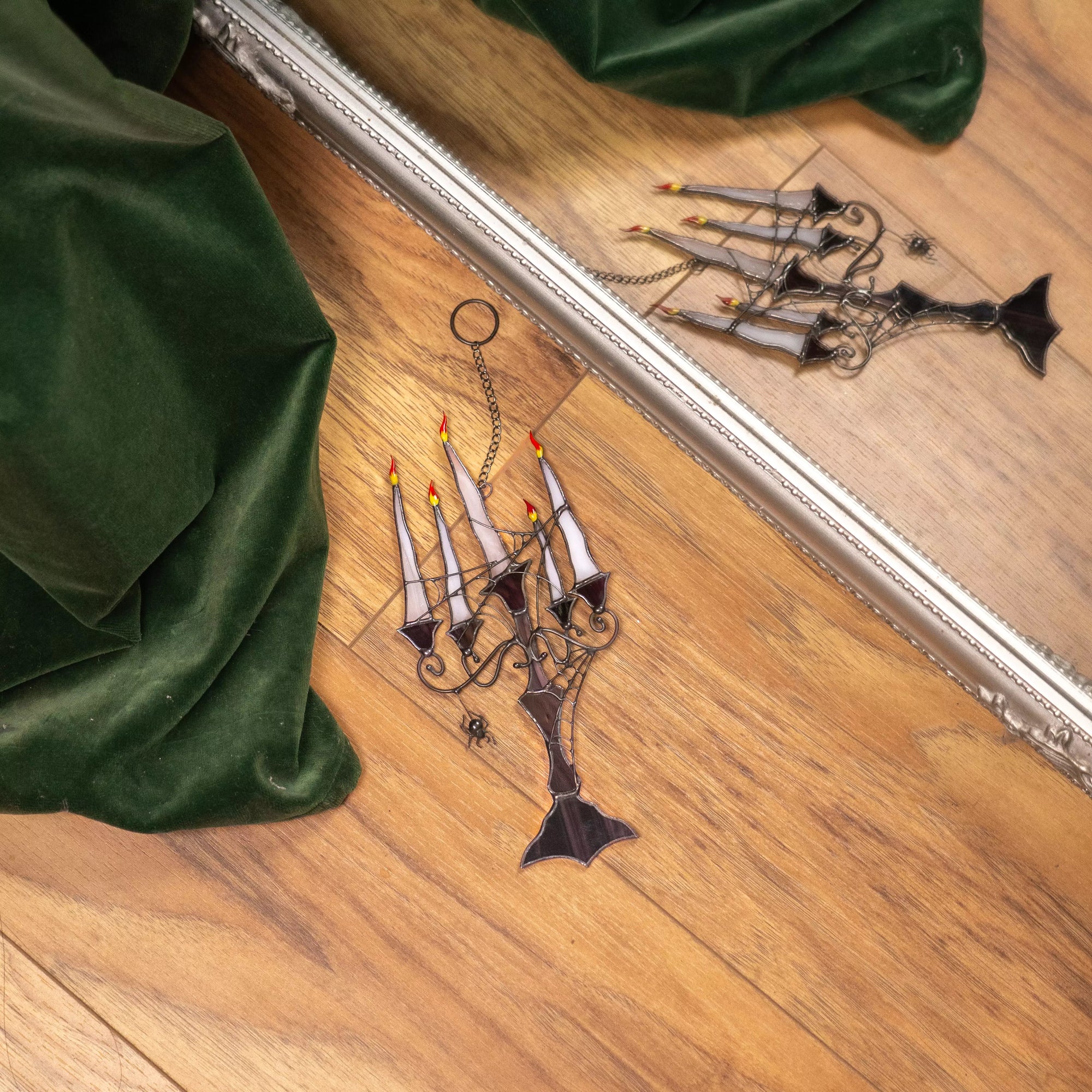 Decorative stained glass candelabra with candles suncatcher on a wooden floor next to green fabric.