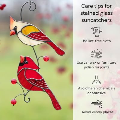 Two stained glass cardinals with red beads hanging in front of care instructions on cleaning and maintenance