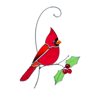 Red stained glass cardinal perched on a metal branch, holding holly leaves and red beads.