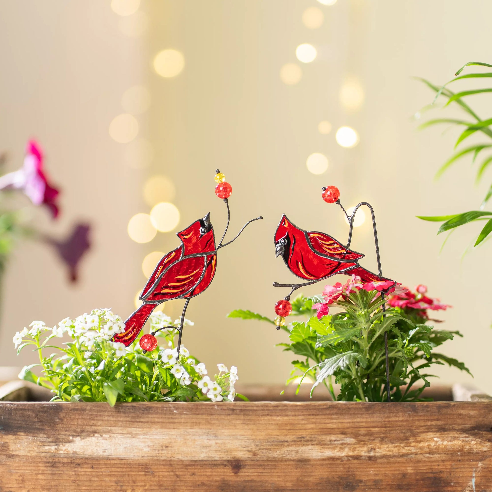 Stained glass cardinal plant stakes on a floral arrangement with a blurred background