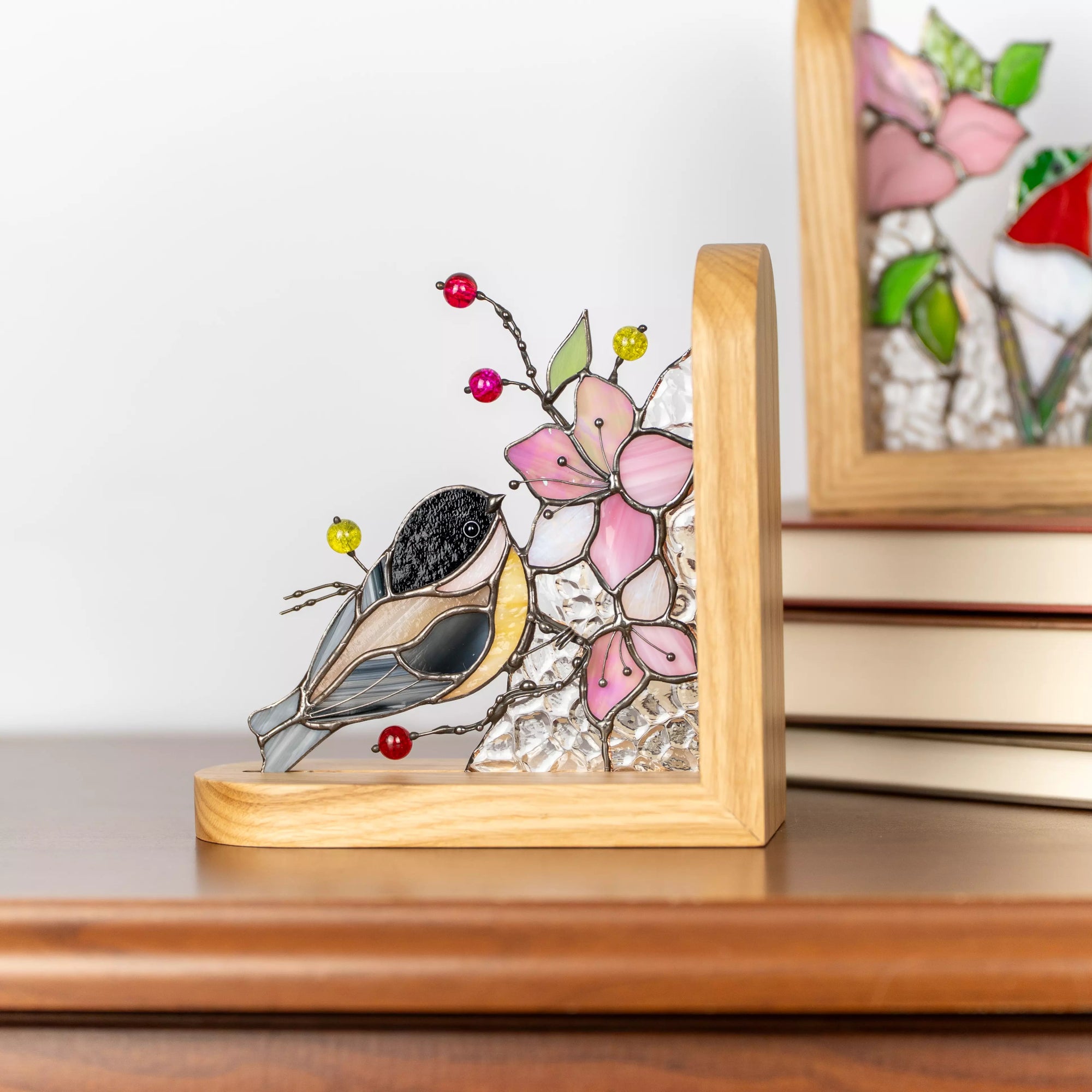 Close-up of stained glass chickadee bird with layered gray, yellow, and blue glass, surrounded by pink flower petals and colorful glass beads.