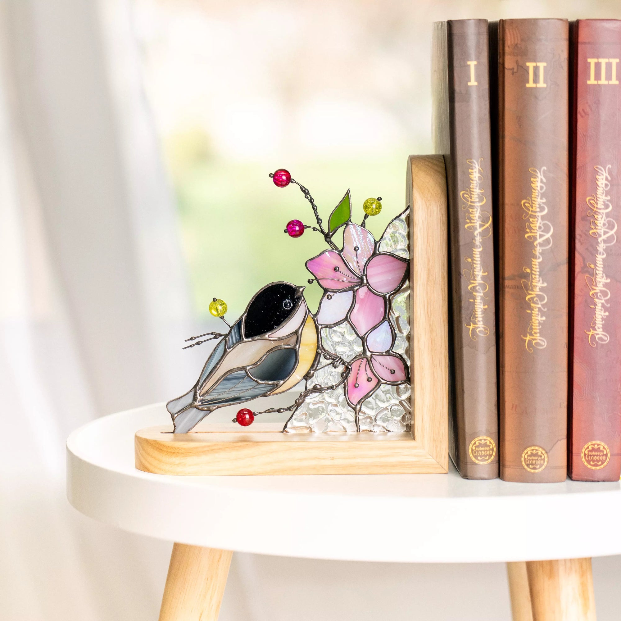 Stained glass chickadee bird leaning toward pink blossoms, accented with red and yellow glass beads, mounted in a smooth wooden bookend base.