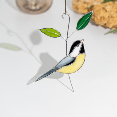 Stained glass chickadee suncatcher with yellow body and green leaves casting a soft shadow on white surface