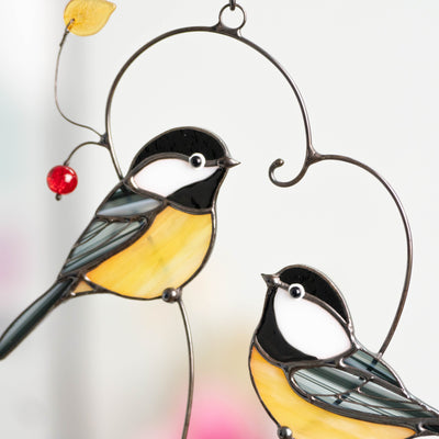 Two handcrafted stained glass chickadees facing each other inside a heart-like metal branch with hanging beads.