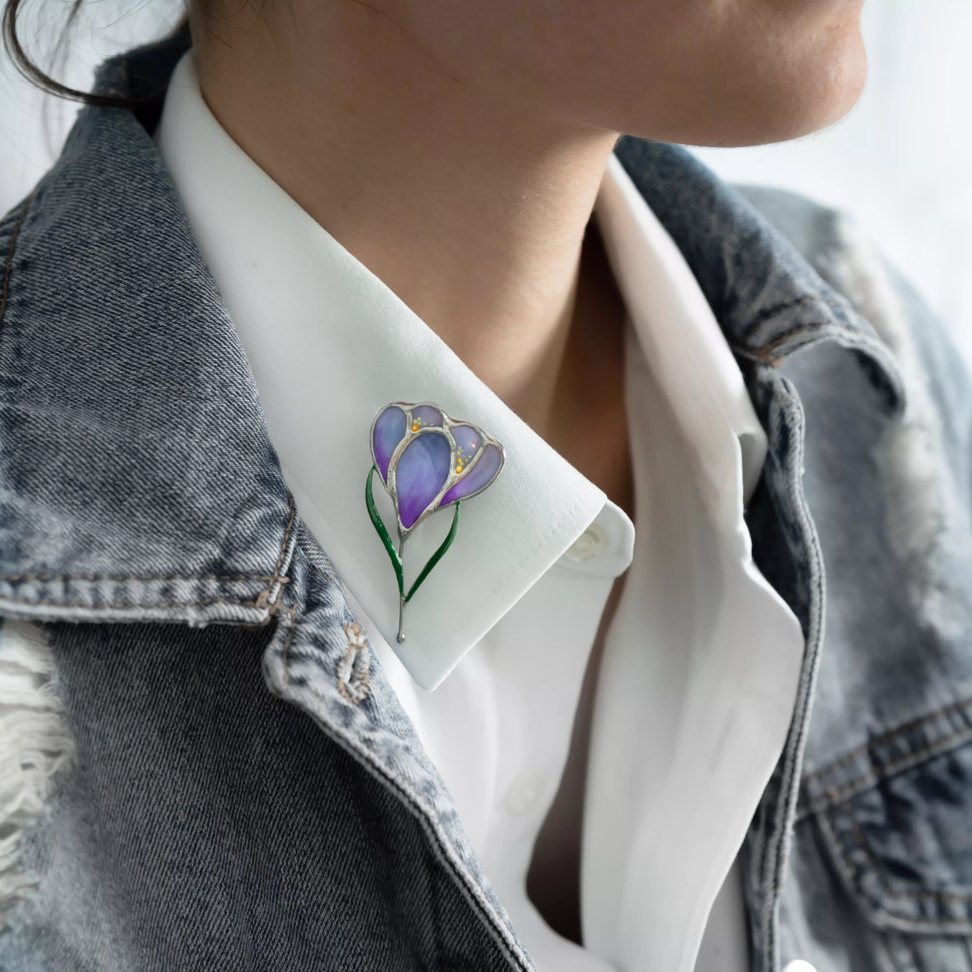Purple stained glass crocus brooch pinned to a white shirt collar and denim jacket, showing elegant floral accent.