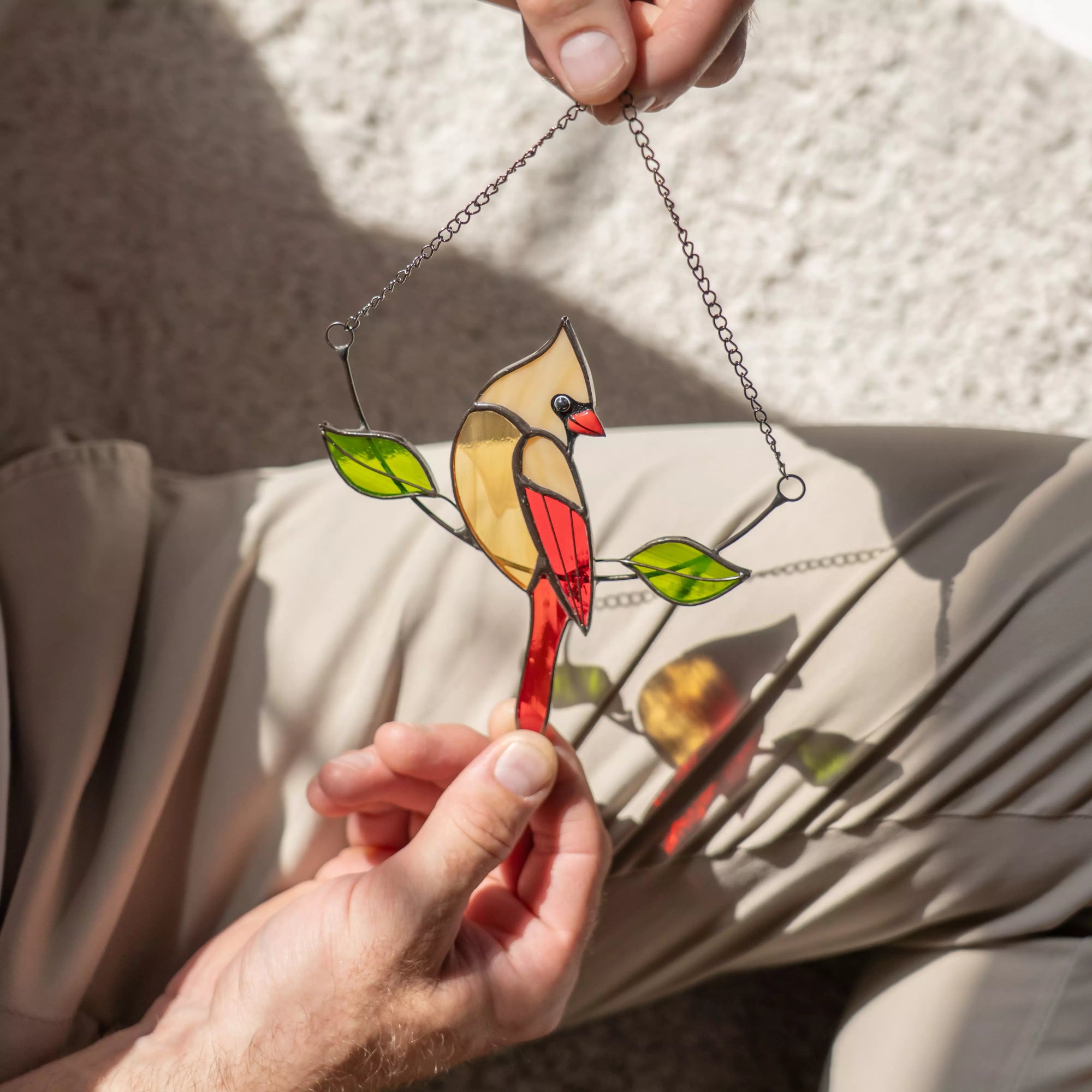 Stained glass female cardinal bird hanging ornament held by a person, casting shadow on a cover 
