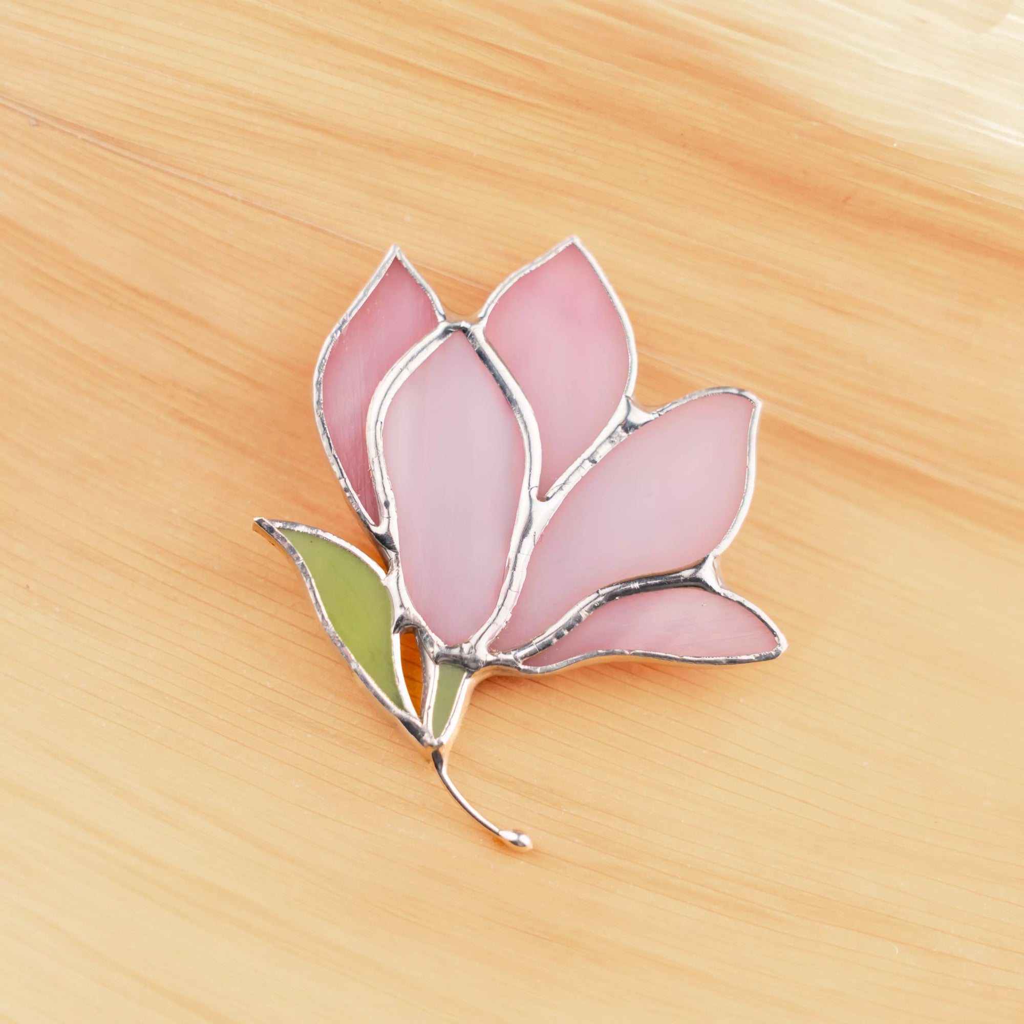 Stained glass magnolia brooch on a wooden surface