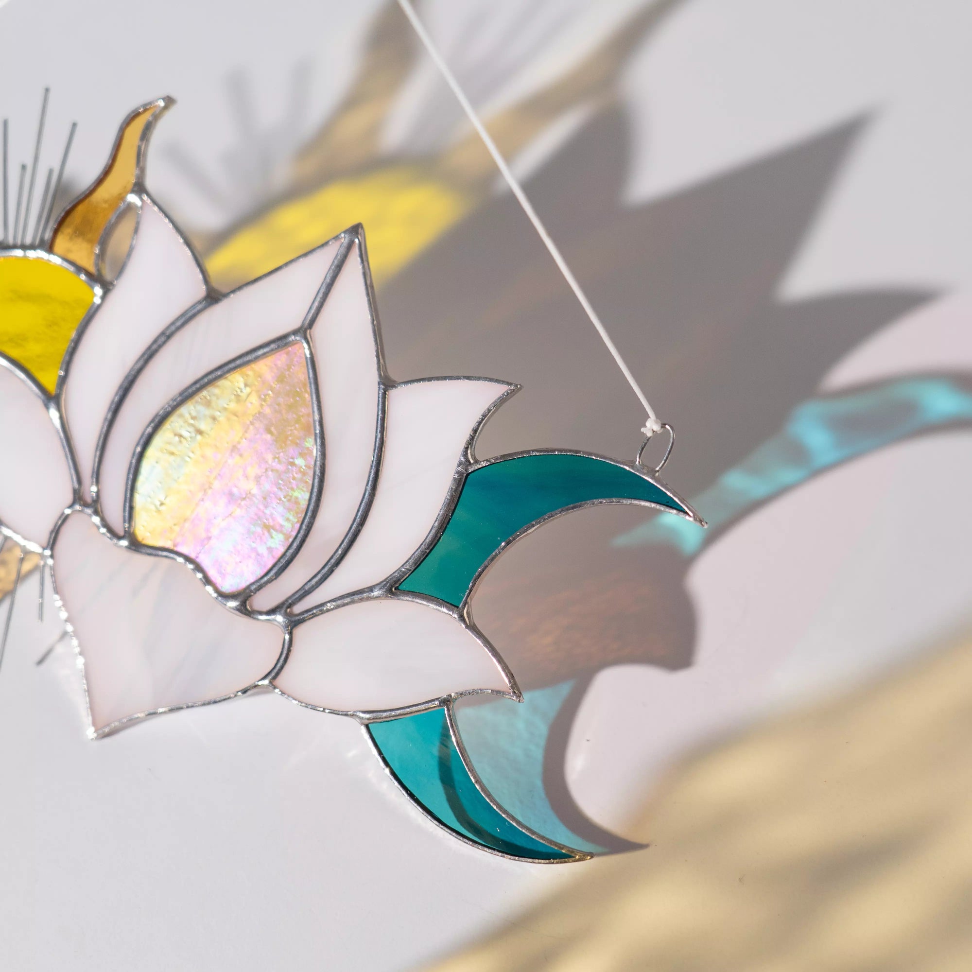 Stained glass lotus flower suncatcher with white, yellow, and blue colors on a light gray background