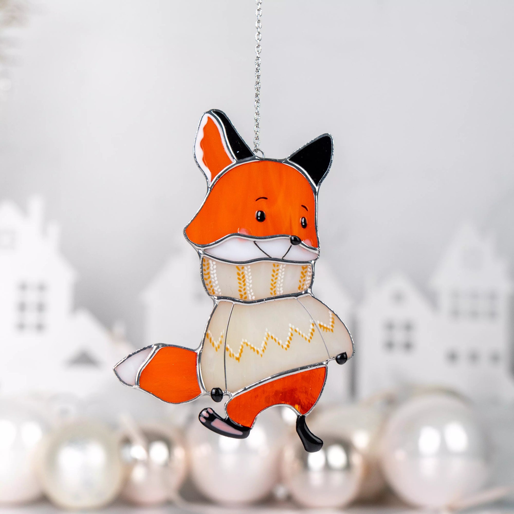 Stained glass suncatcher fox in a sweater ornament hanging against a blurred decorative background