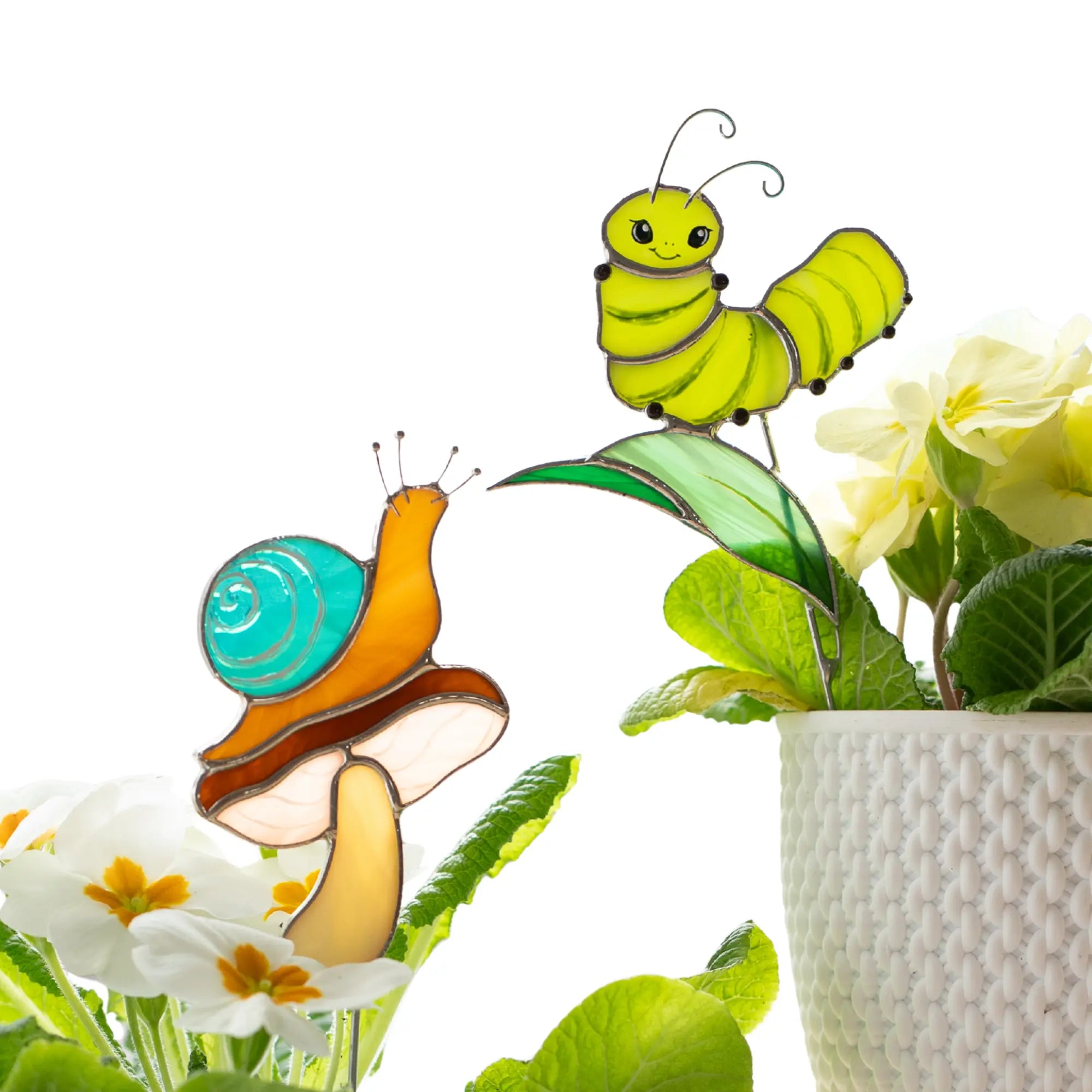 Stained glass garden stakes with a snail on a mushroom and a green caterpillar held by a person against a white background.