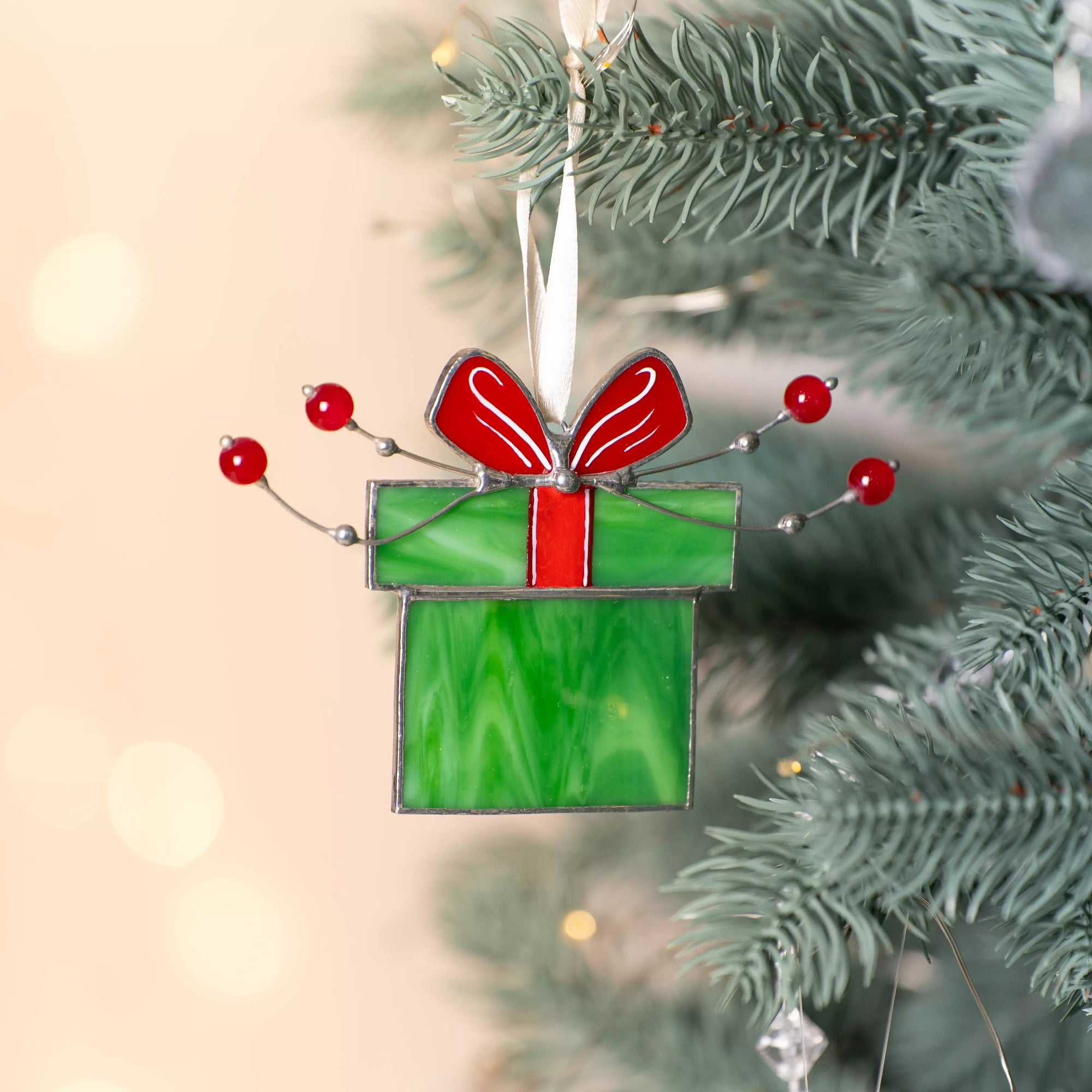 Stained glass Christmas gift box with red bow, red berries, and green accents hanging on Christmas tree